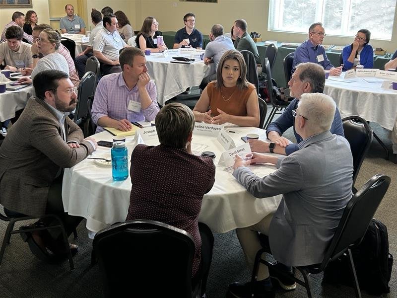 A group of professionals seated around a round table engaged in discussion at a conference or workshop.