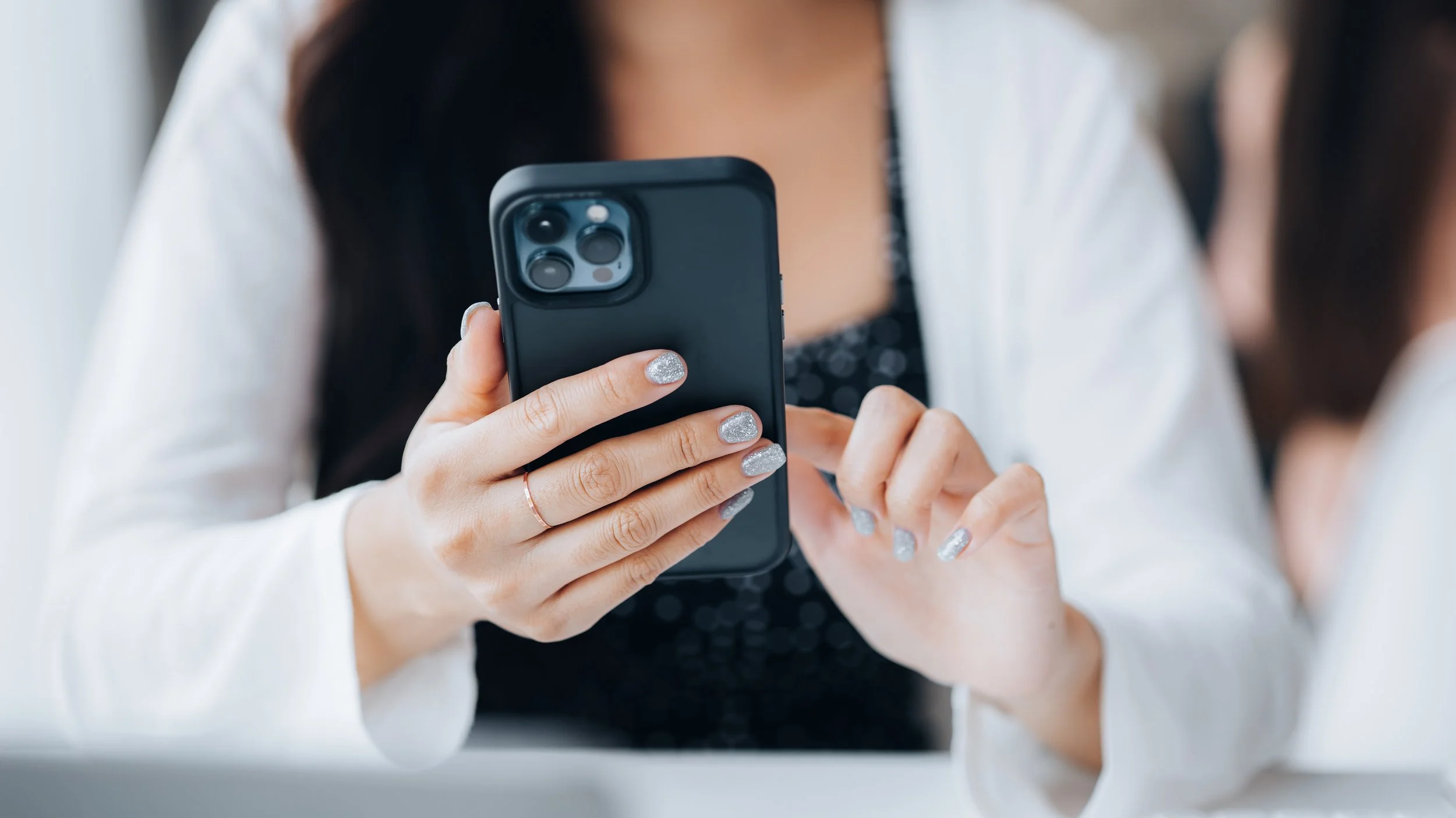 A woman with manicured nails holding a black smartphone with a triple-lens camera in a close-up shot.