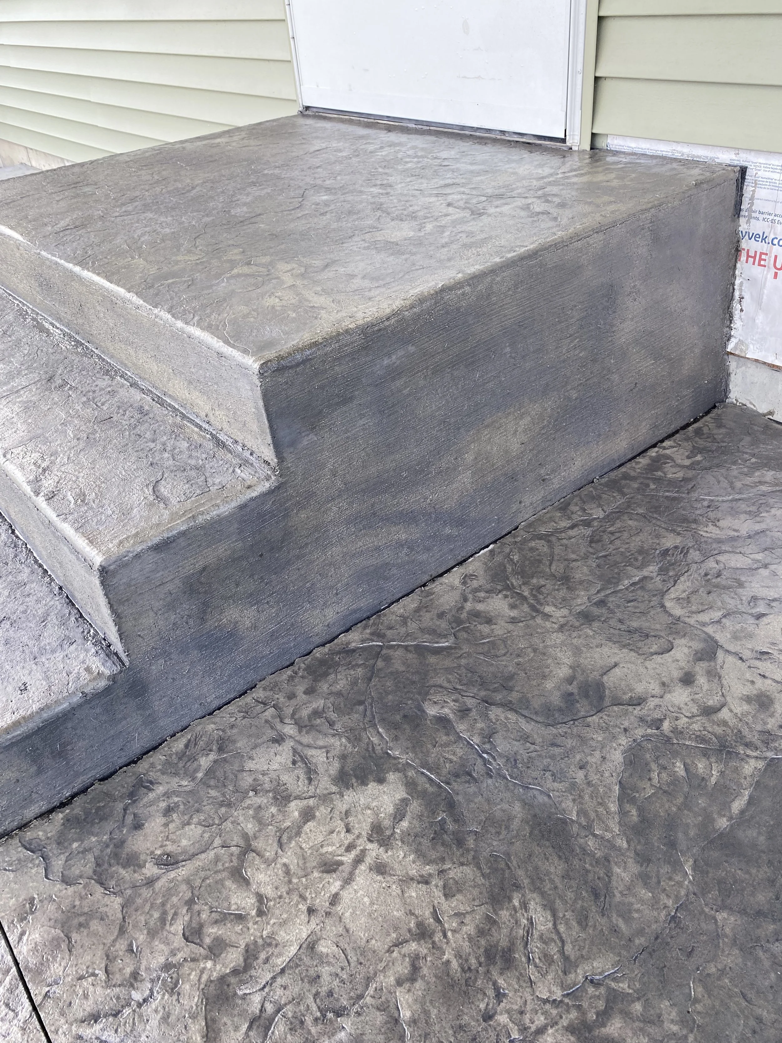 Concrete front steps with a textured surface leading up to a door at a house.