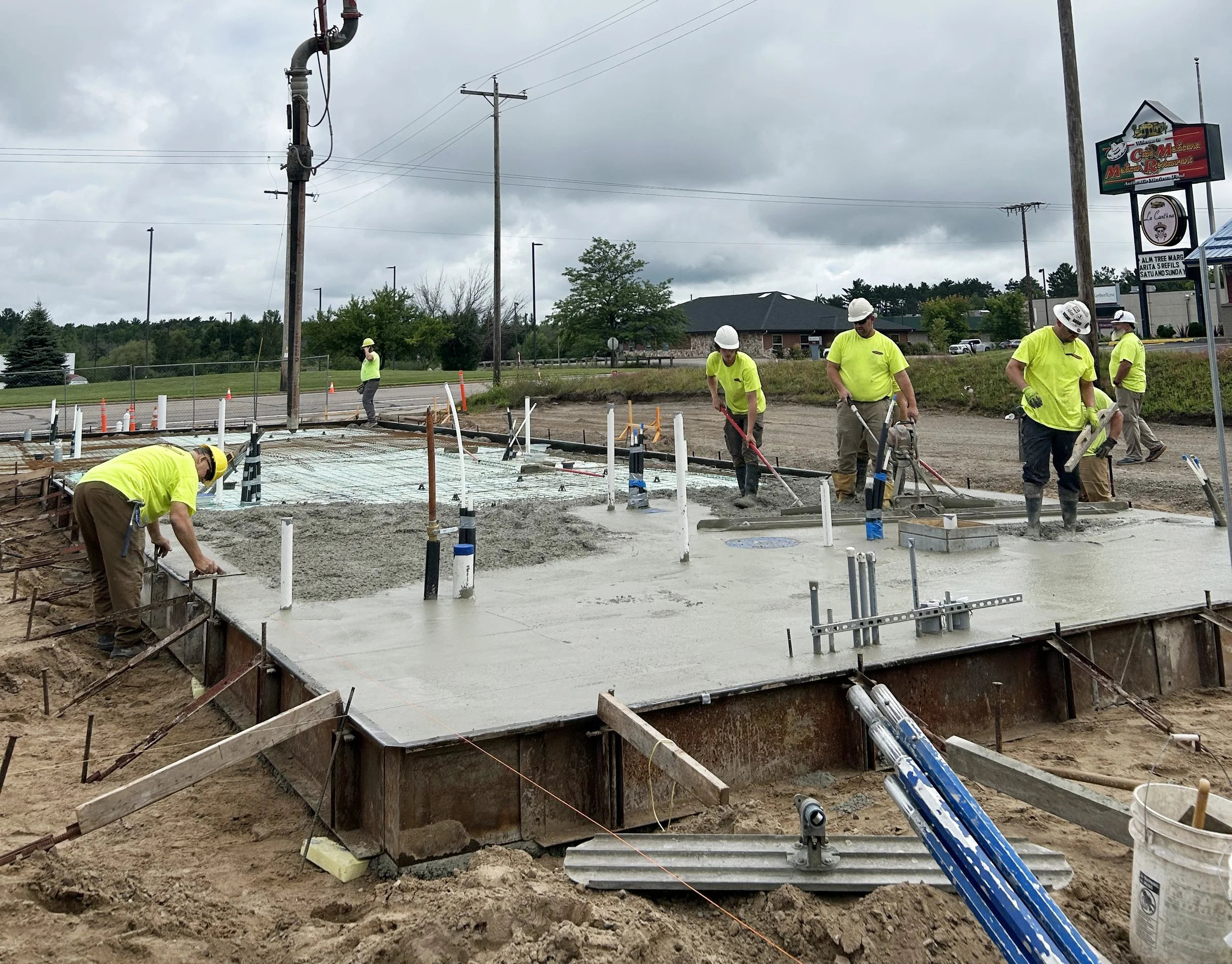 Construction workers pouring and smoothing concrete on a building foundation with safety gear and construction tools.