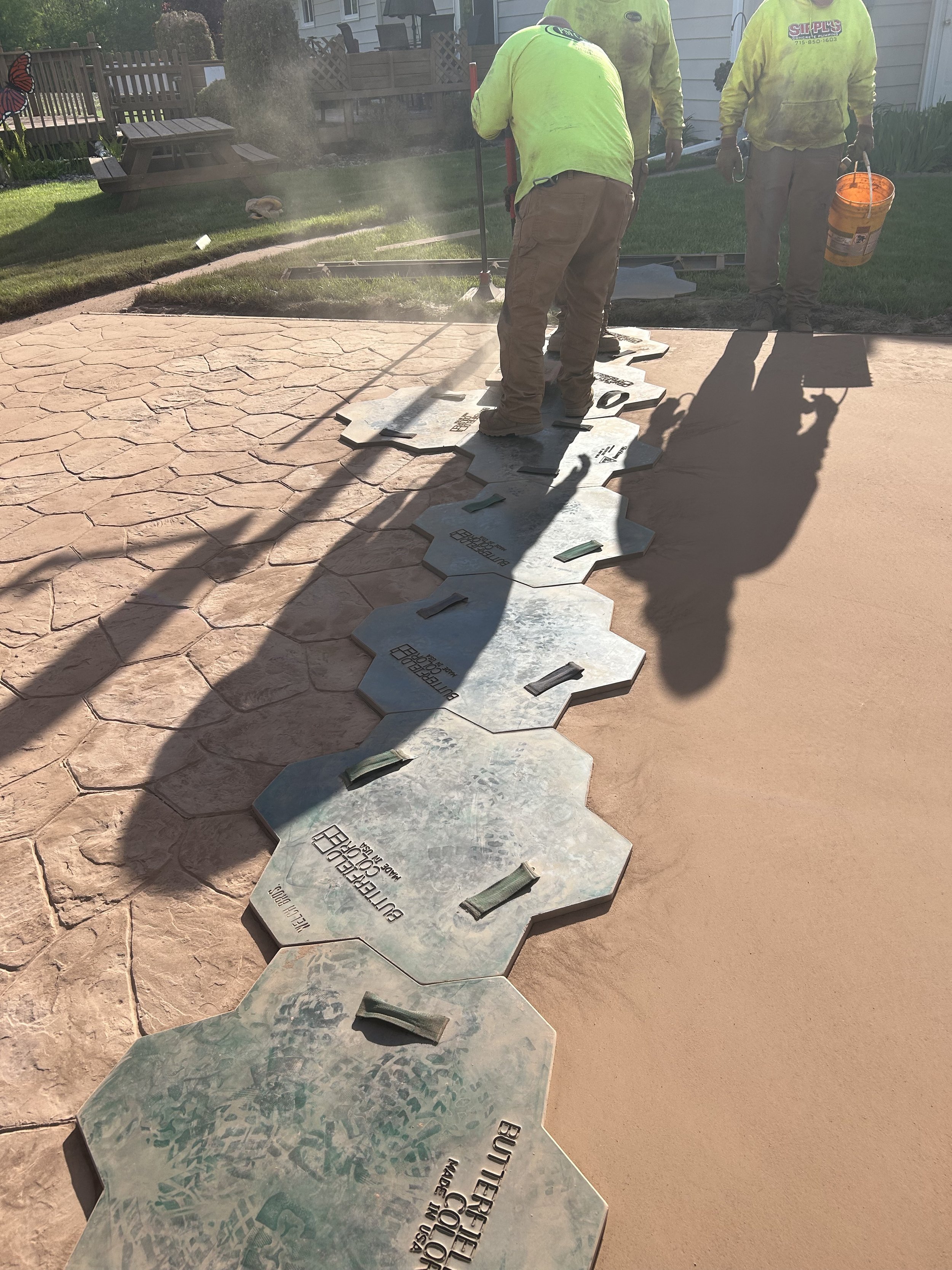Workers installing decorative concrete pavers on a pathway in a backyard.