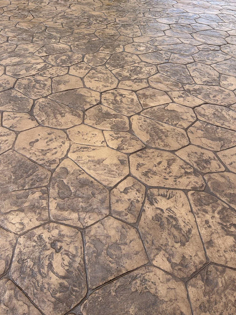 Close-up view of a patterned concrete or stone floor with irregularly shaped stones in shades of brown and tan.