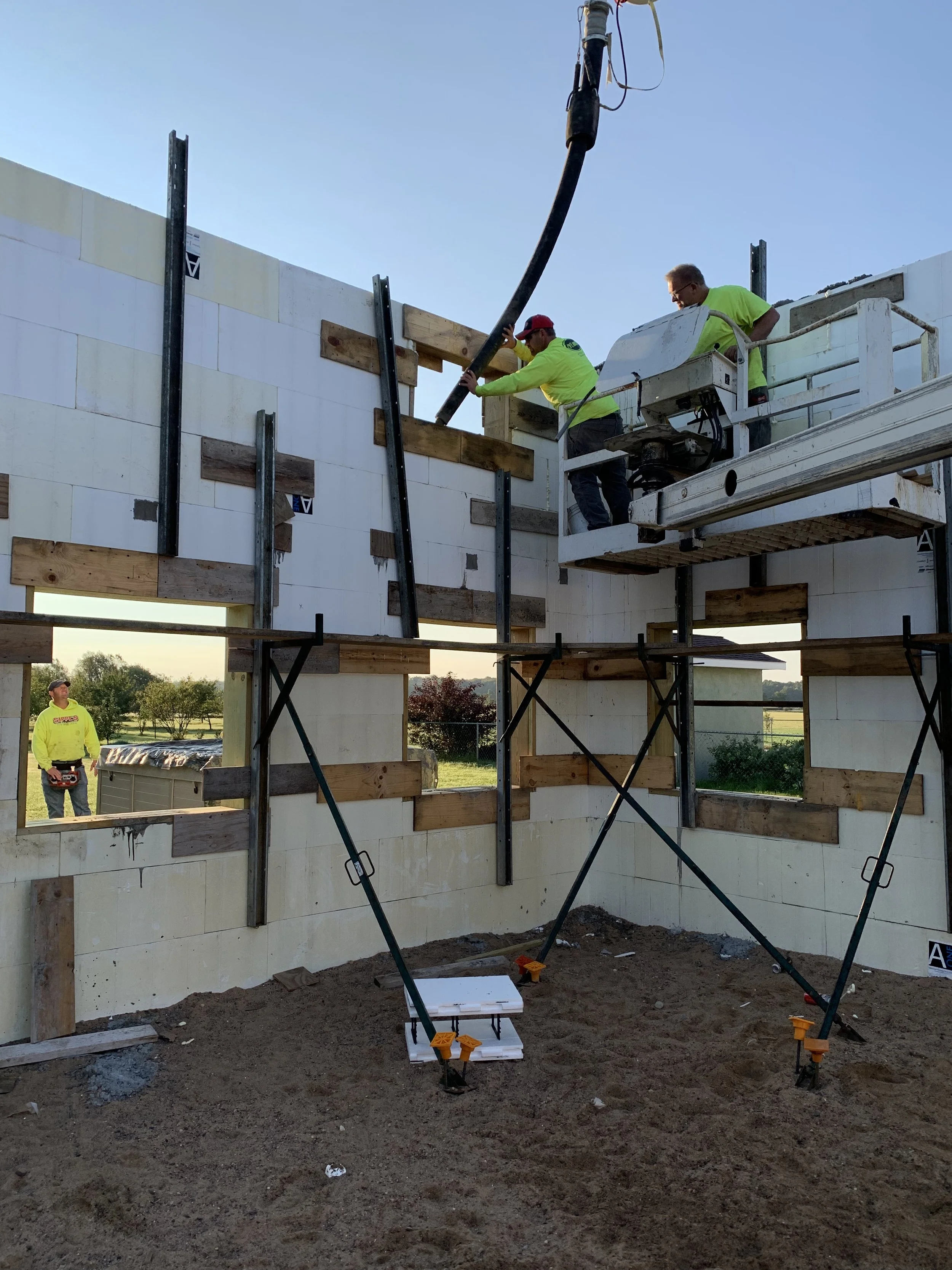 Construction workers building the walls of a house using concrete blocks, with scaffolding and a crane for assistance, during daytime.