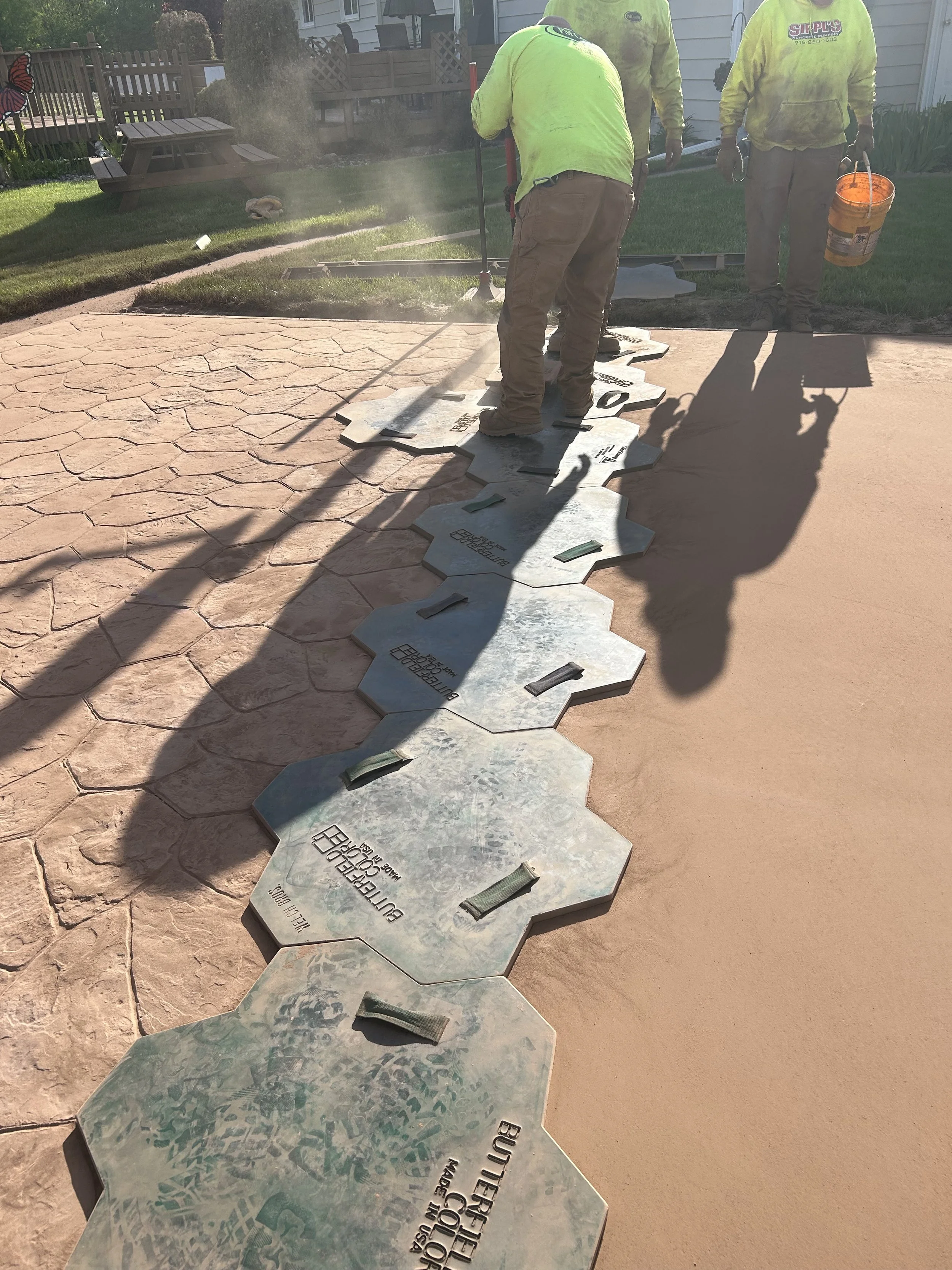 Workers installing decorative tile pathway in a backyard, with tools and construction materials visible.