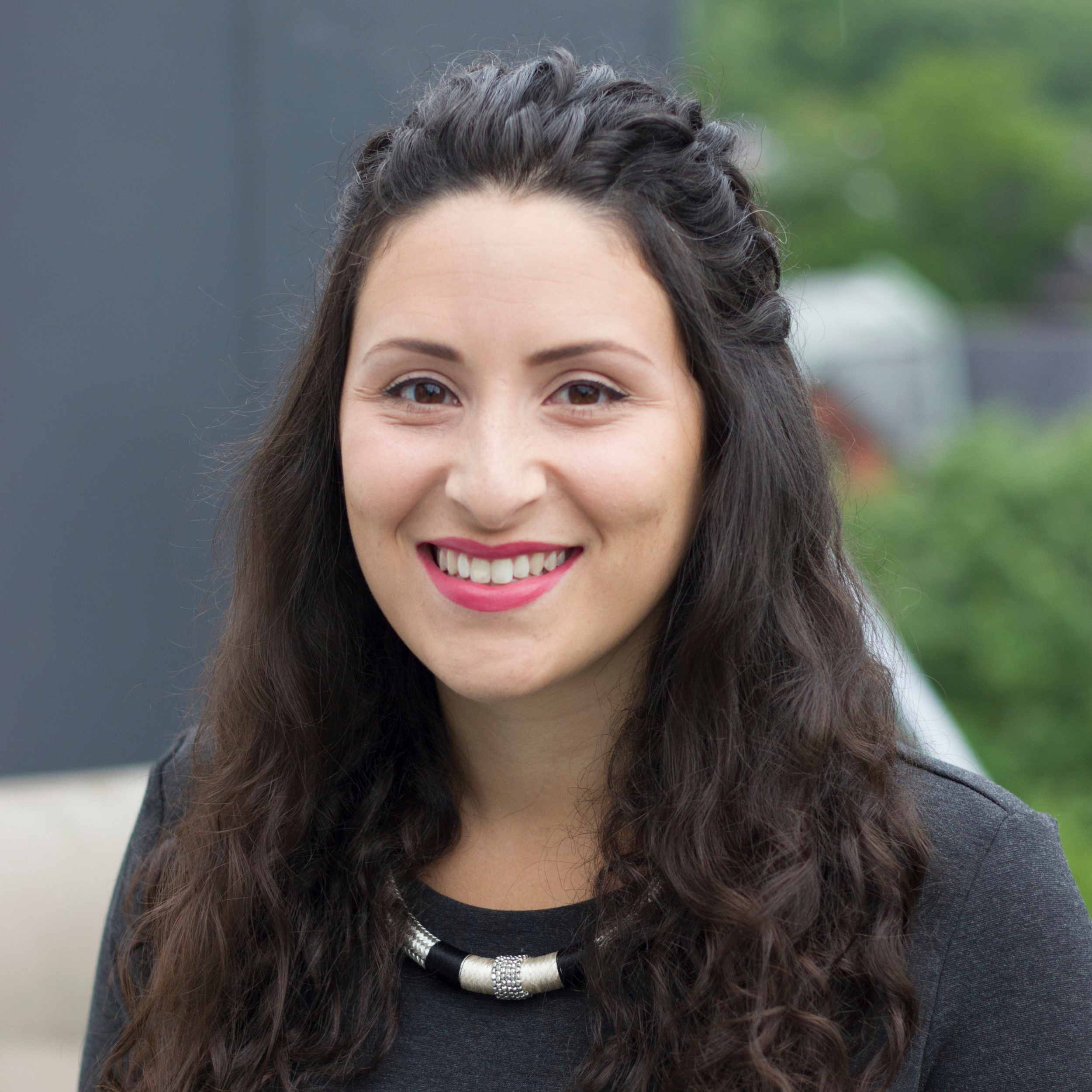 Natalia Ontario-based licensed psychologist providing client-centered support and mental health services across all life stages at Stillpoint Psychology. A woman with long, curly dark hair, smiling,  outdoors with blurred greenery in the background.