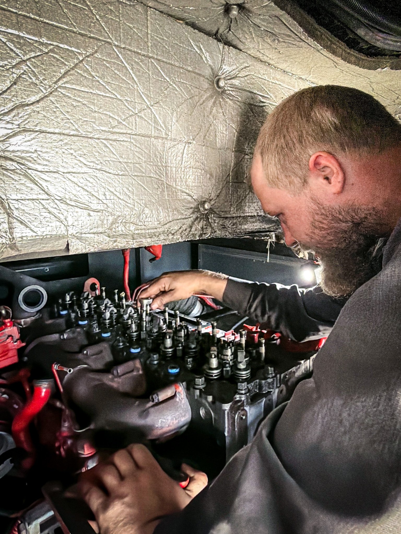A man working on a car engine, adjusting valves or parts with his hand.