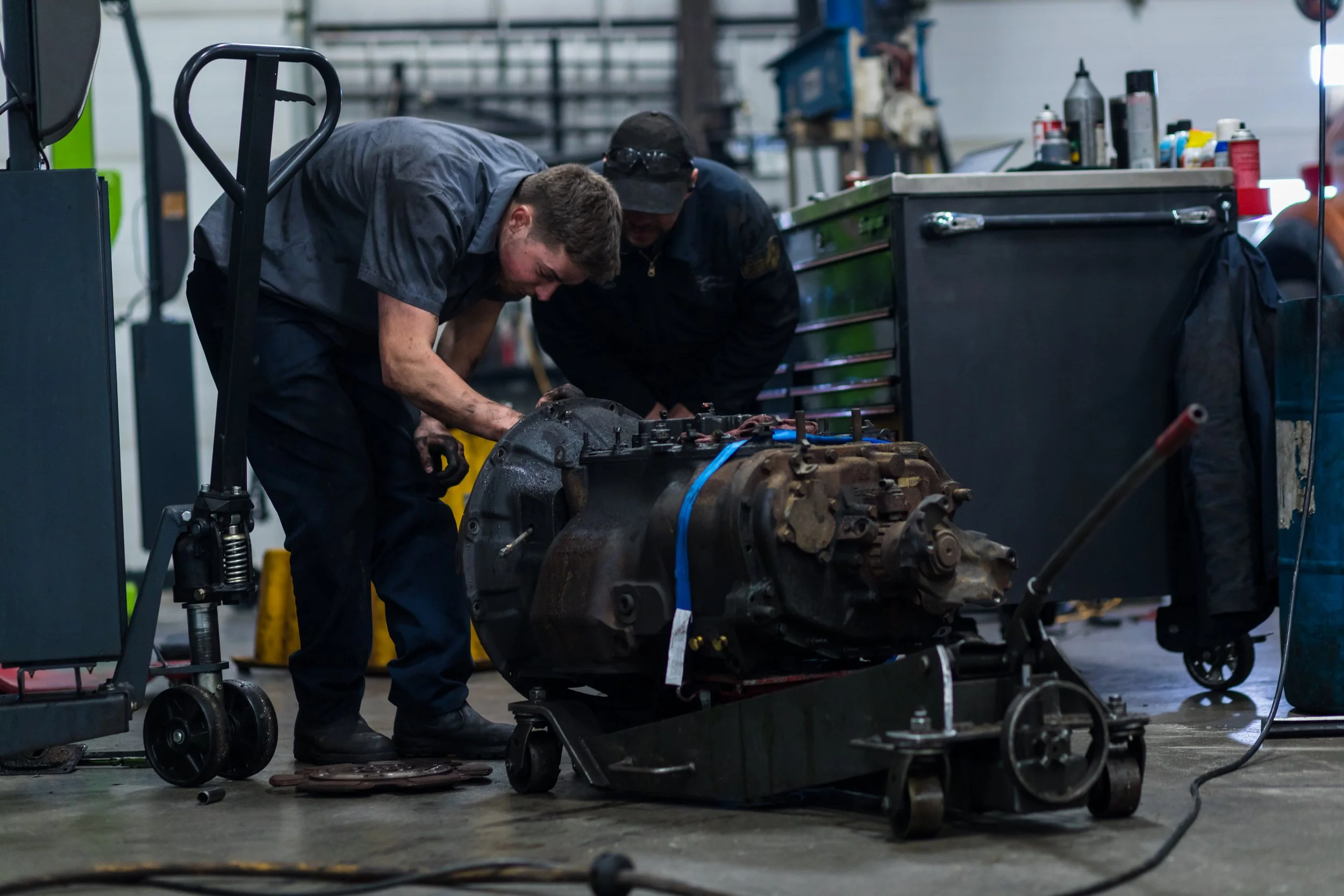 Two mechanics working on a car engine in a garage, surrounded by tools and equipment.