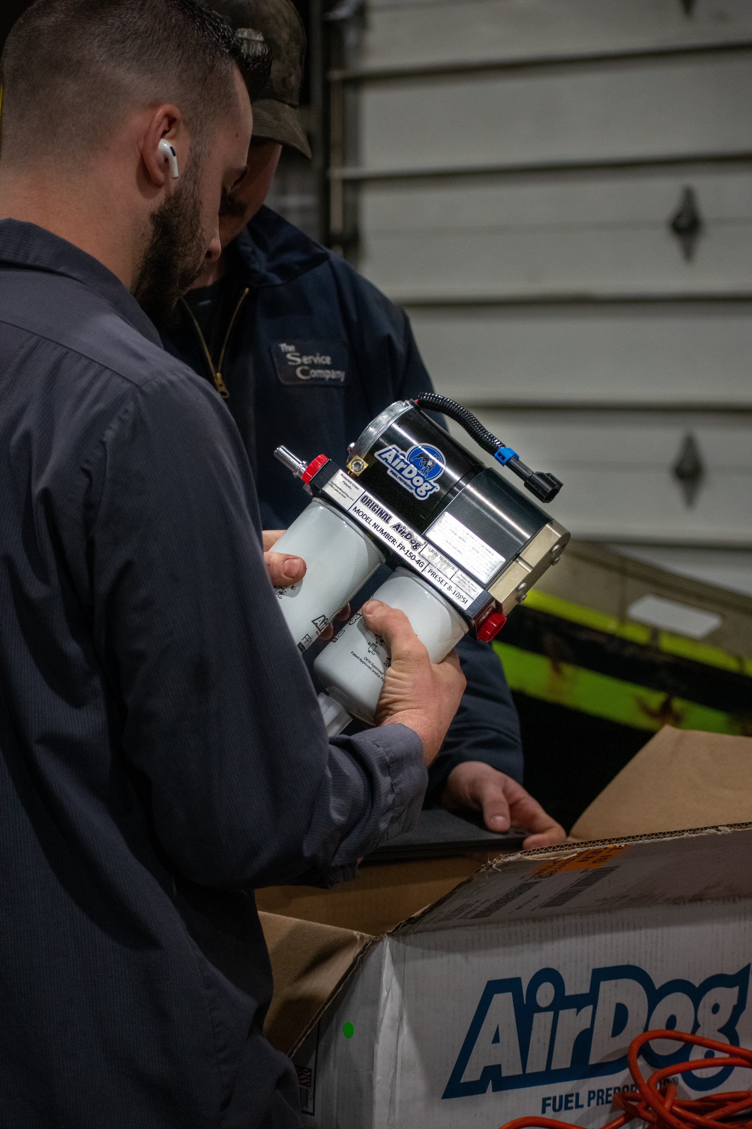 Two men inspecting a fuel filter with an AirDog logo in a warehouse or garage.