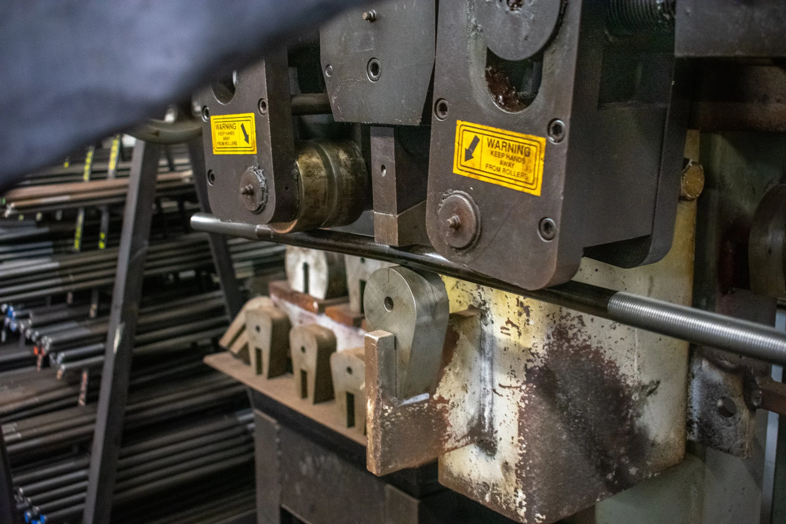 Close-up of industrial machinery with warning labels, metal parts, and bolts, used in manufacturing or metalworking.