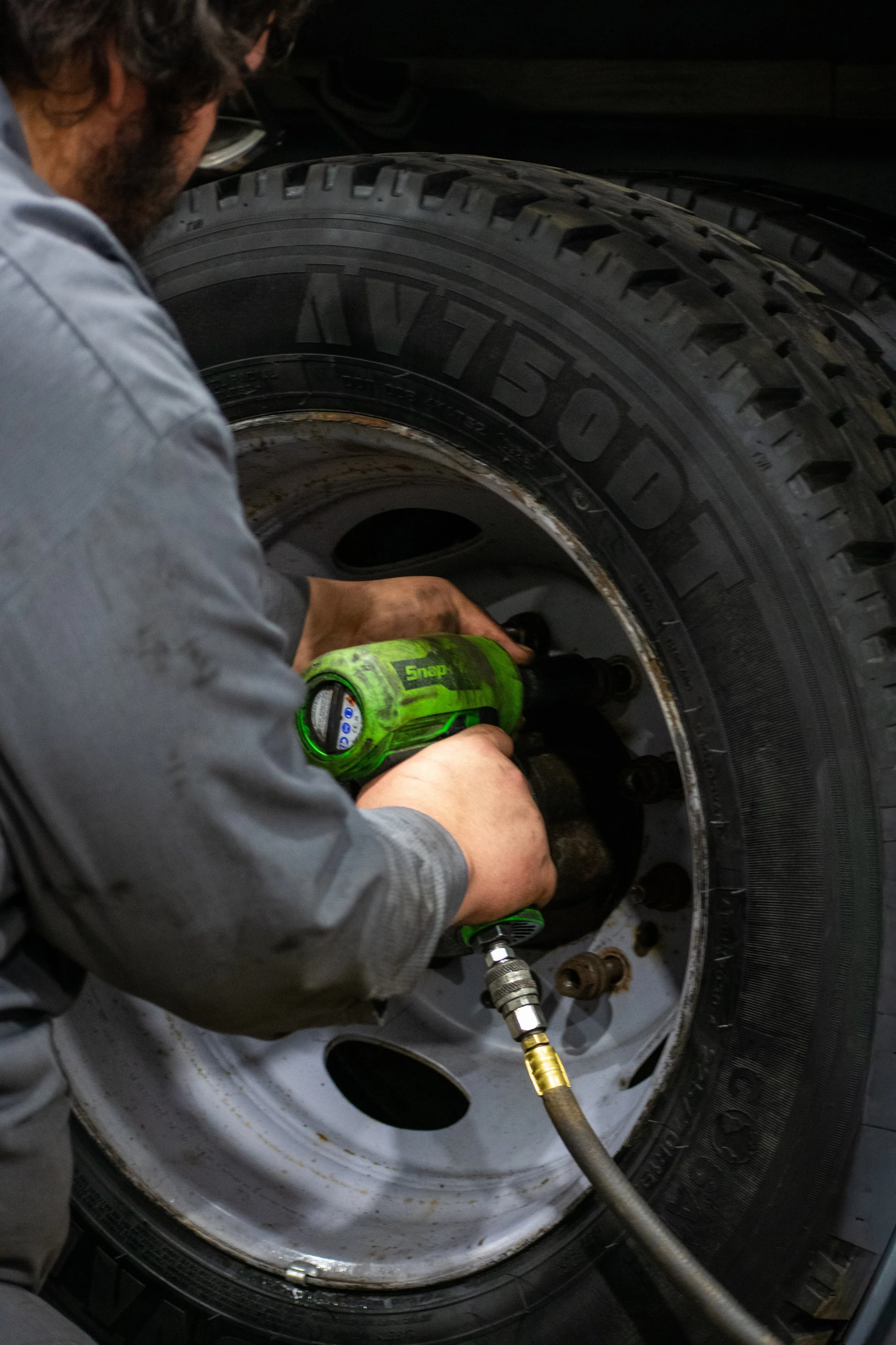 A mechanic is repairing or installing a tire on a vehicle, using a power tool to secure the wheel bolts.