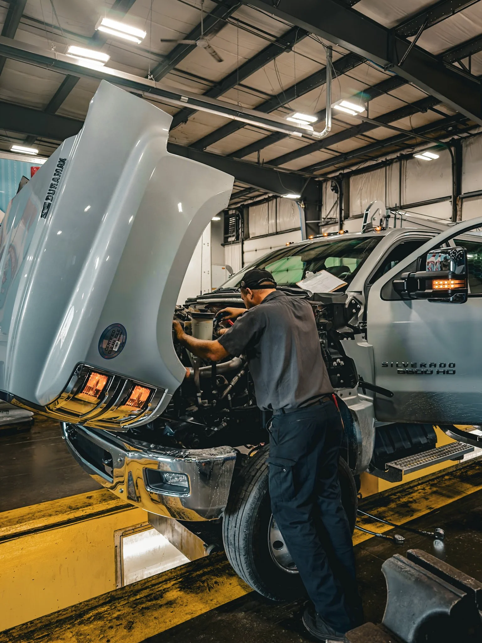 A mechanic working on the engine of a Silverdo truck inside a garage with the hood raised.
