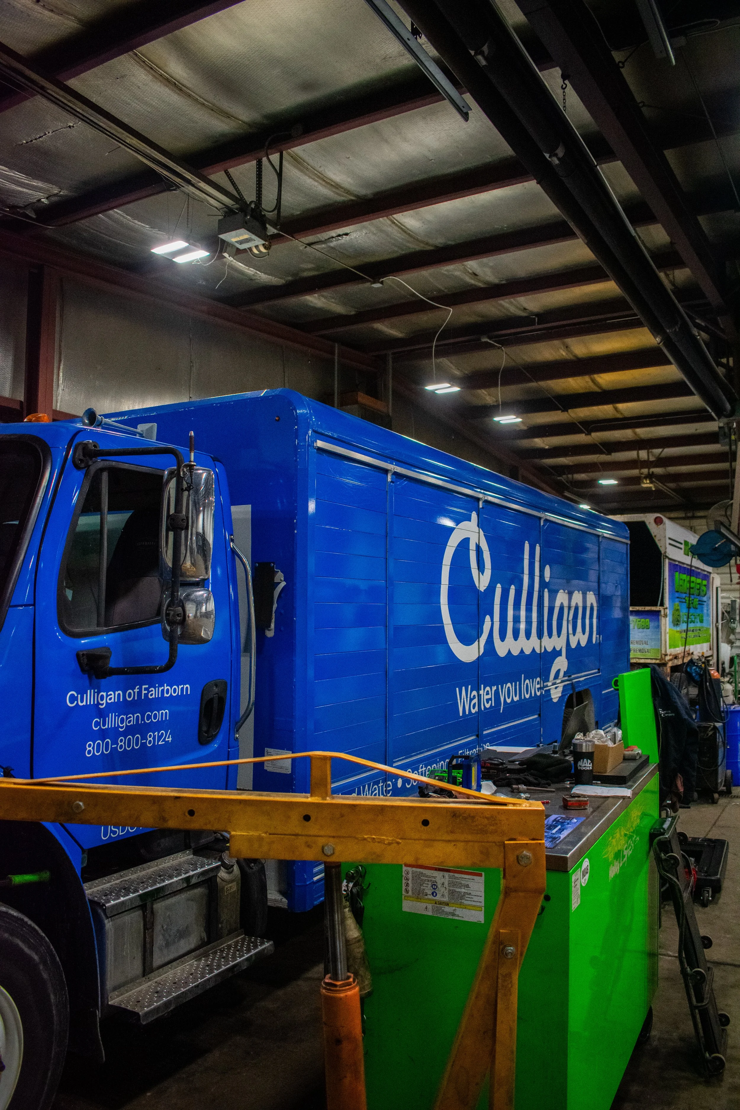 Blue Culligan water delivery truck inside a warehouse, with tools and equipment nearby.