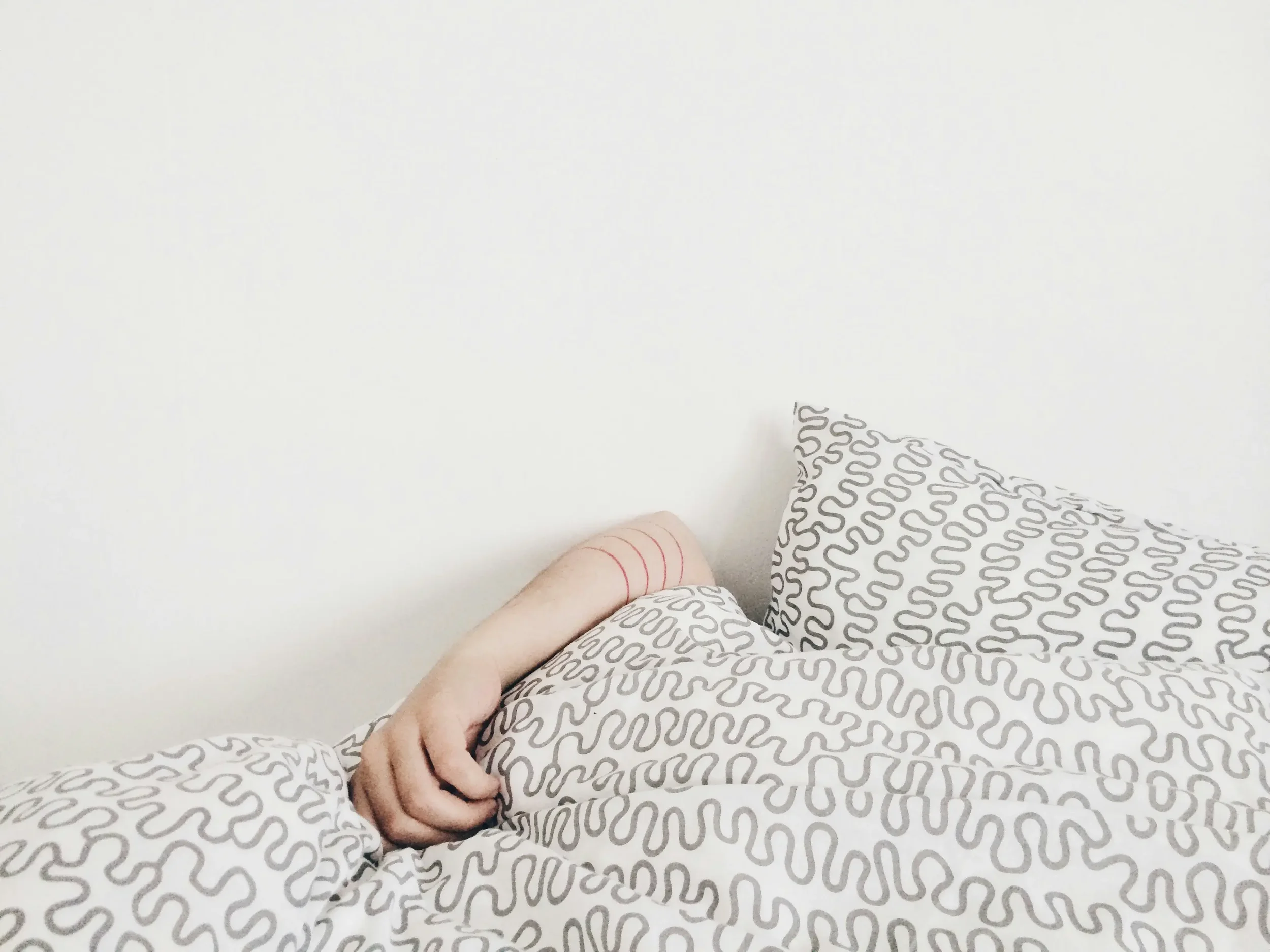 A person reaching their arm out of bed from under the covers