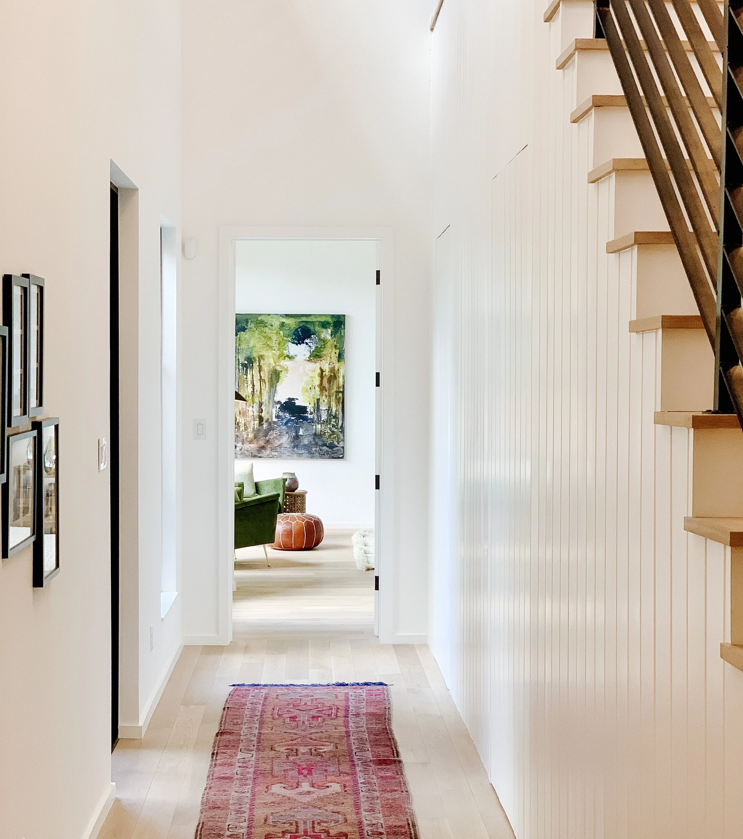 A hallway view leading into a living room with artwork, green chair, and pouf.