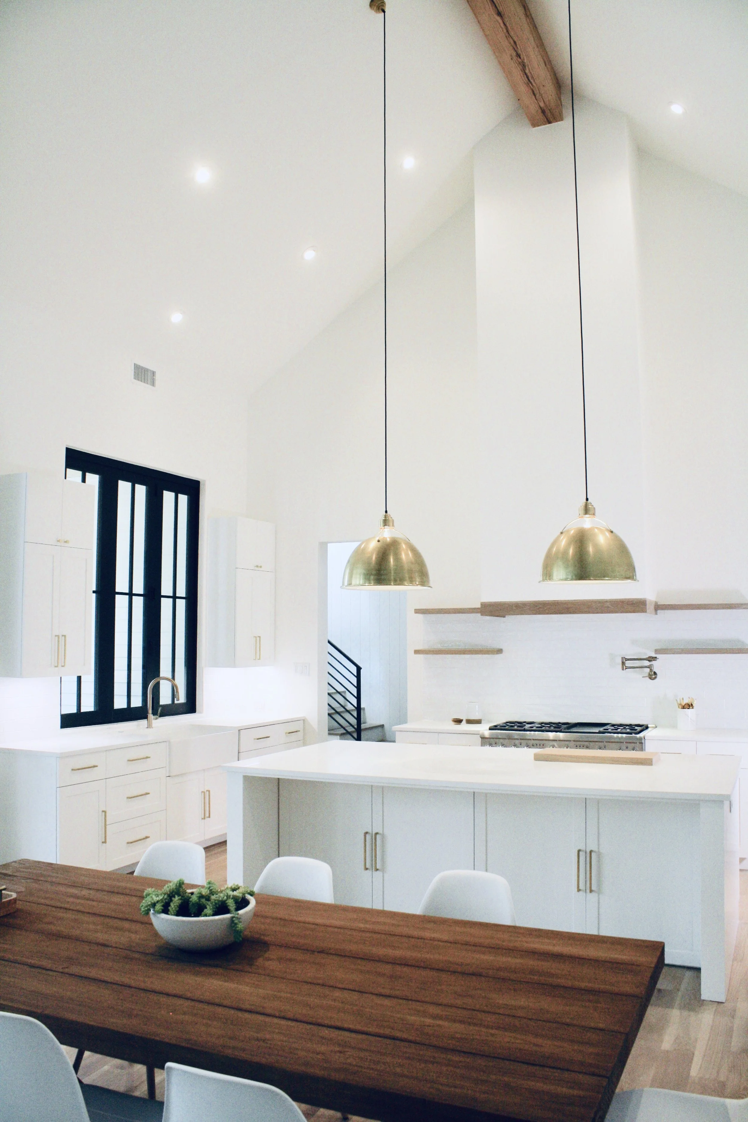 Modern kitchen with white cabinets, a large island, wooden accents, and two gold pendant lights hanging from a vaulted ceiling.