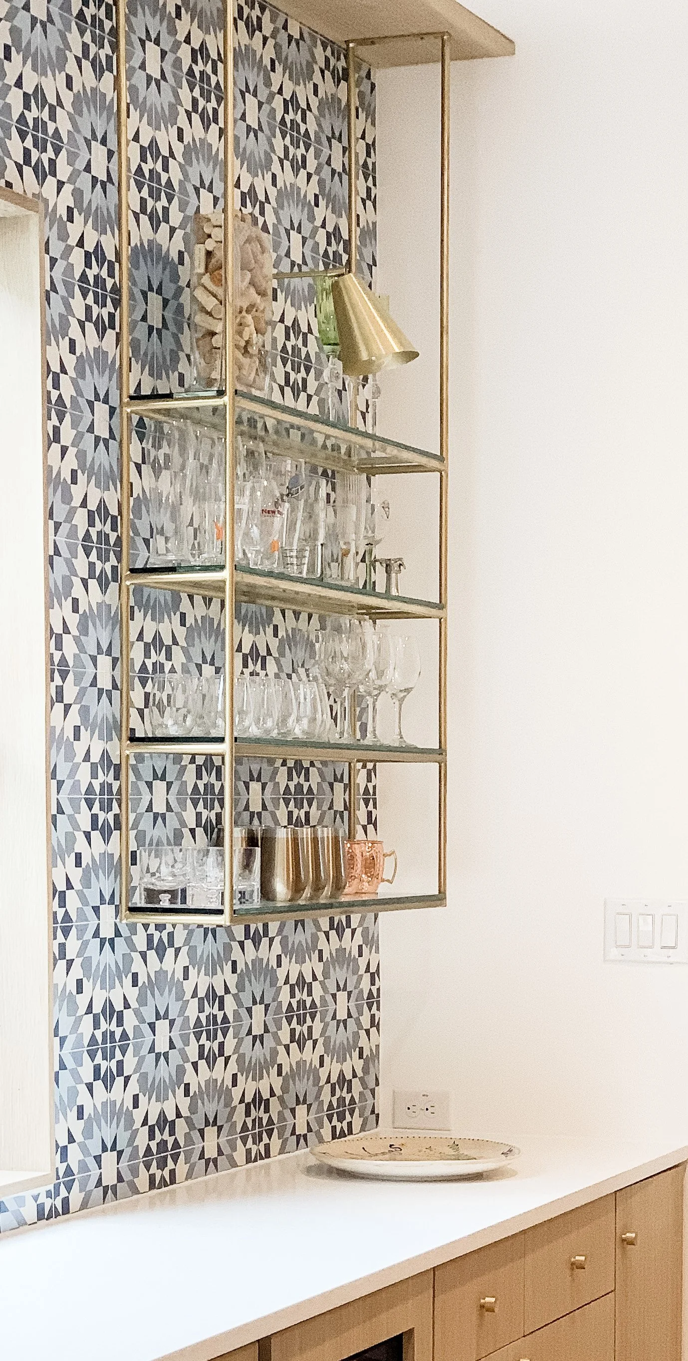 A modern kitchen shelf with glassware against a patterned tile background.