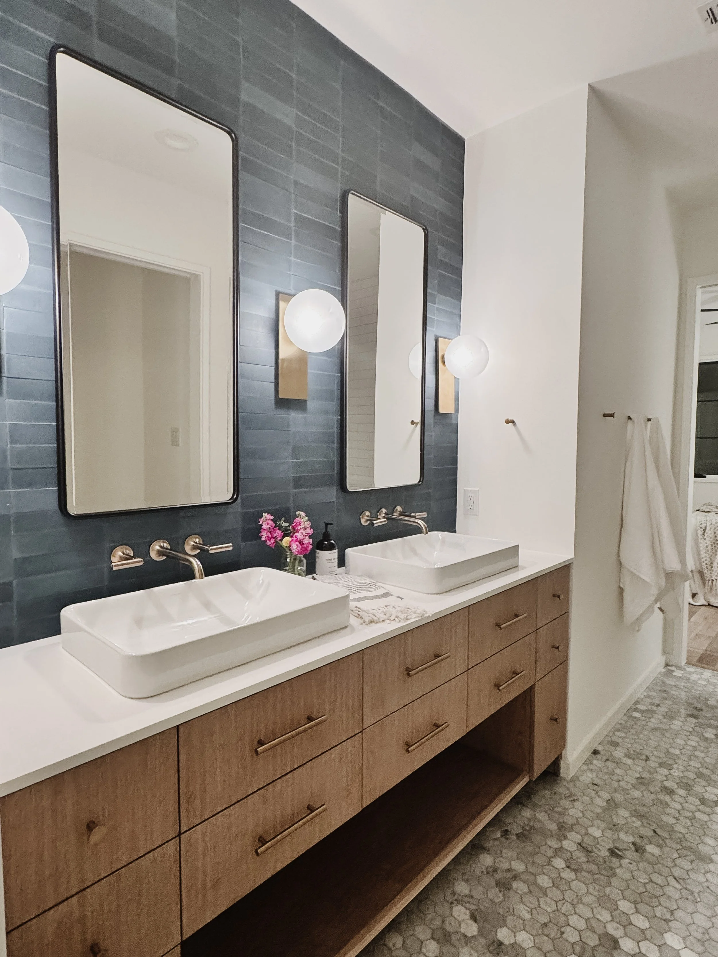 Modern bathroom with double vanity, two vessel sinks, two rectangular mirrors, hexagonal tile floor, blue tiled wall, and wall-mounted lights.