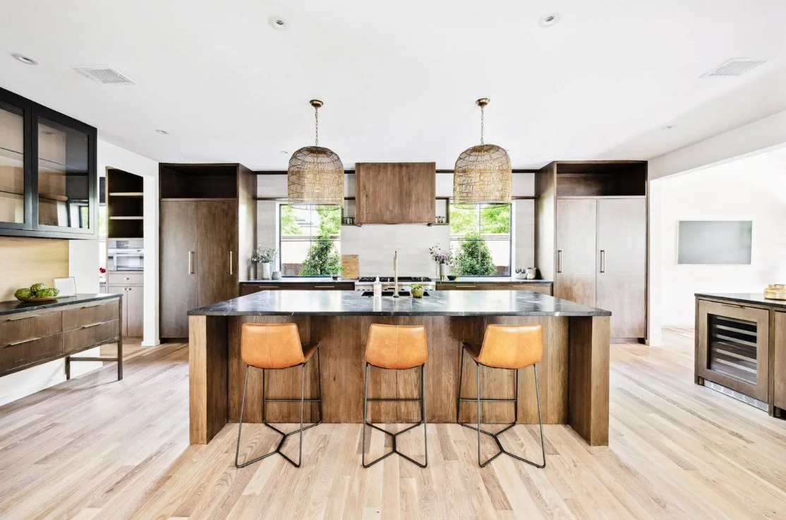 Modern kitchen with a large island, wood cabinetry, and three barstools, with pendant lights and large windows for natural light.