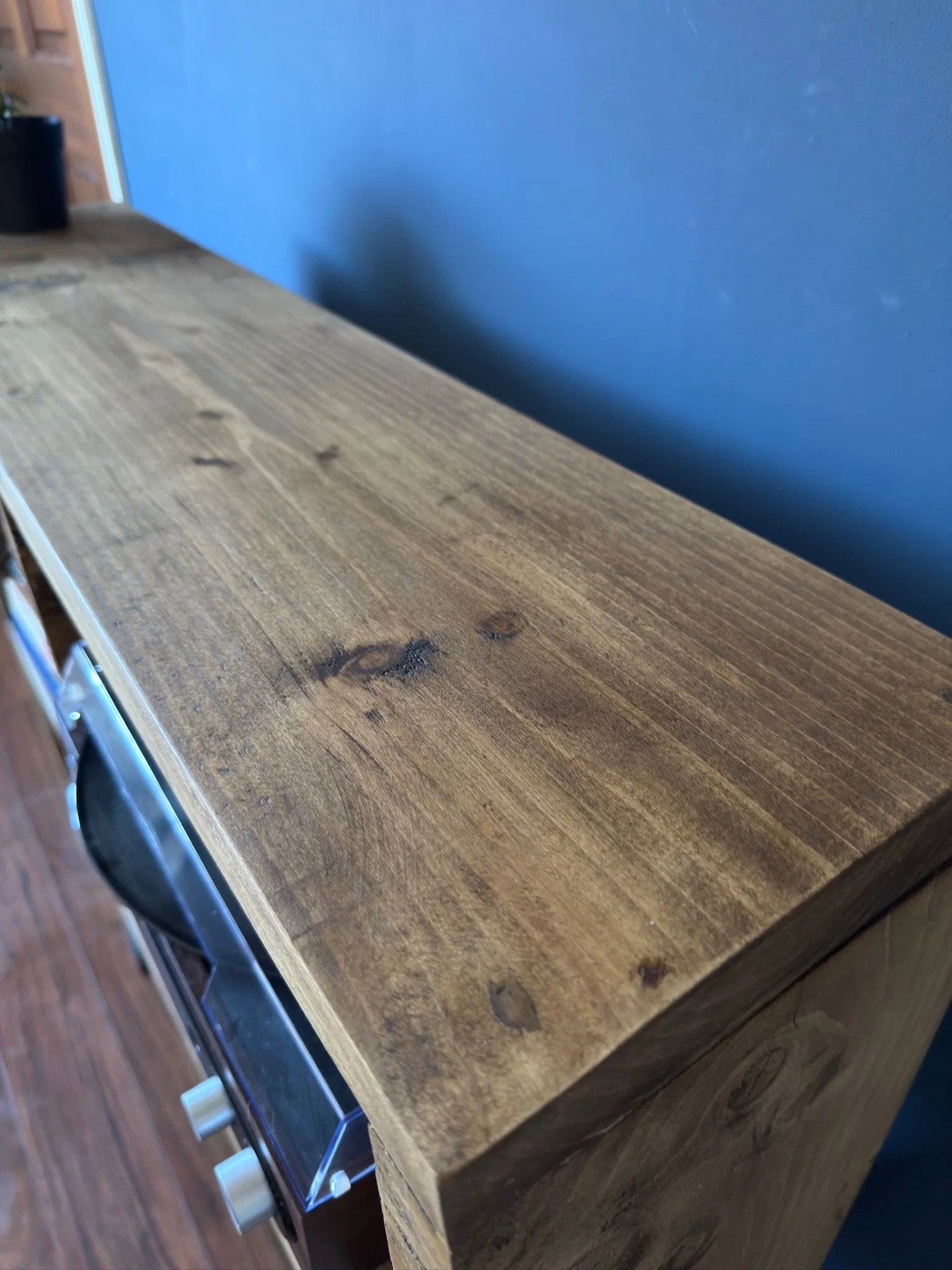 Close-up of a wooden countertop or furniture with knots and grains, against a blue wall.