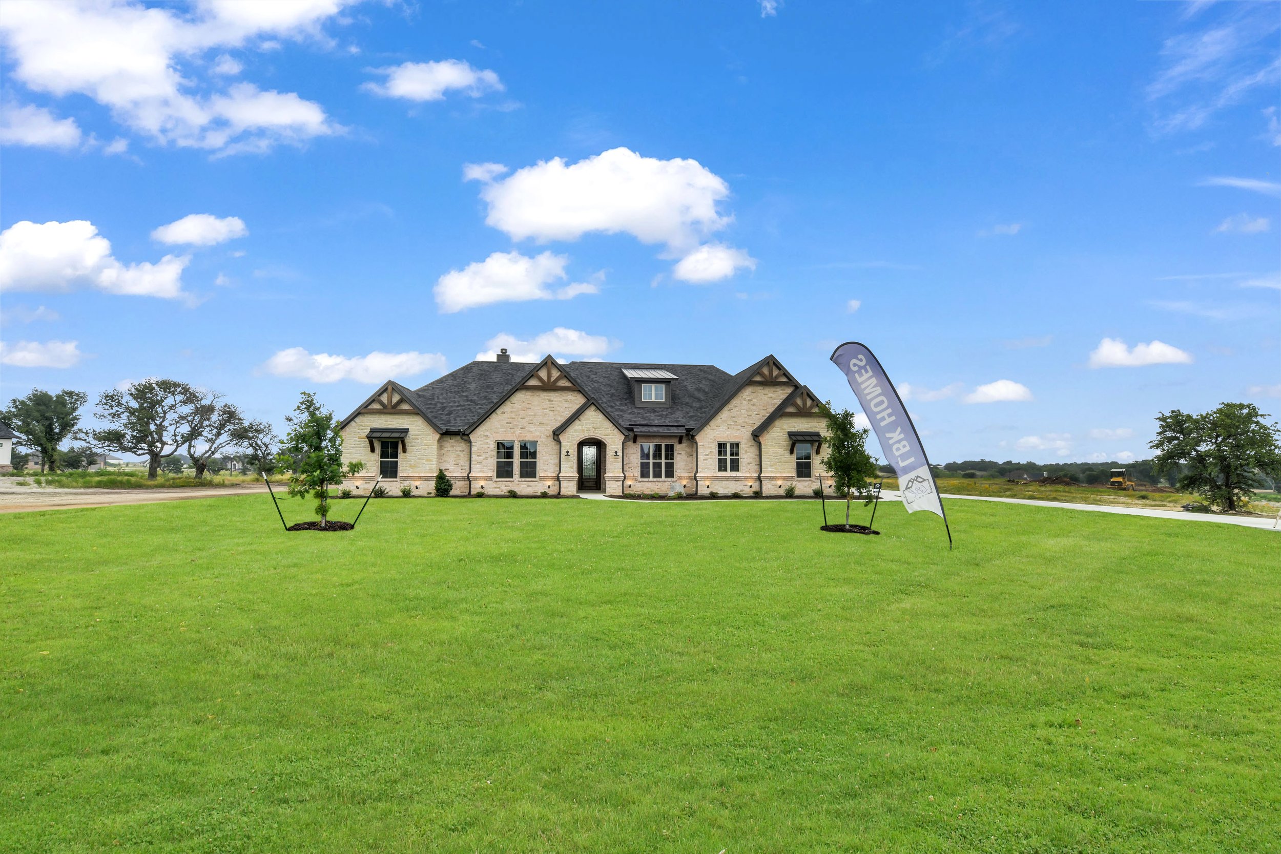 New house on a large green lawn under blue sky with some clouds, with a banner reading 'BUY HOMES'