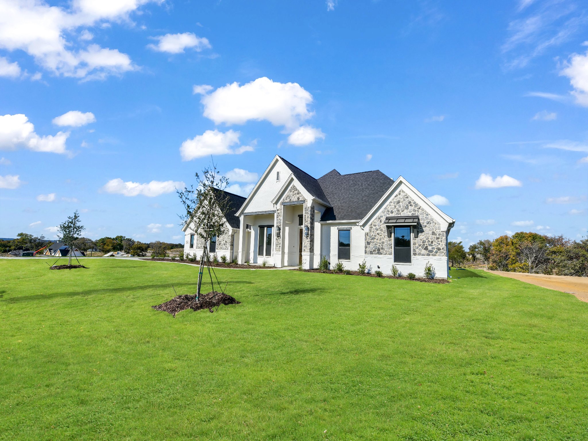 White house with stone accents on a green lawn under a blue sky with white clouds.