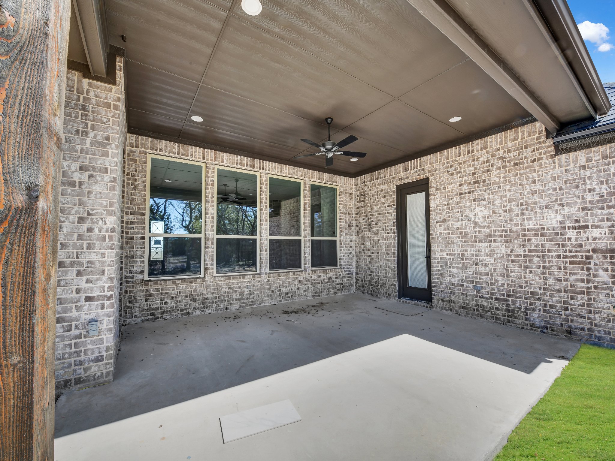 Empty covered patio area with brick walls, a ceiling fan, multiple windows, a door, and a concrete floor.