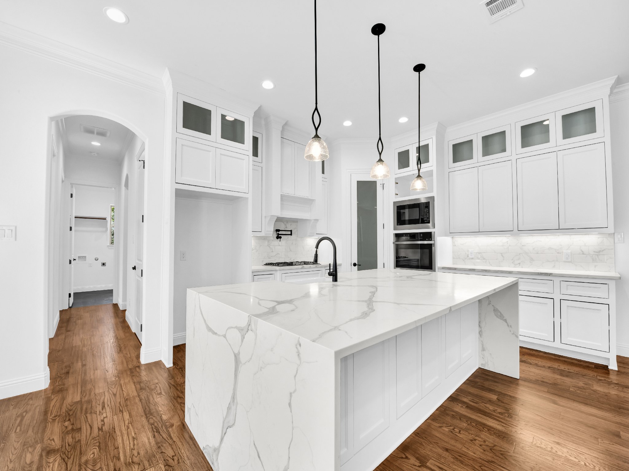 Modern white kitchen with marble island, wooden floors, built-in appliances, and pendant lighting