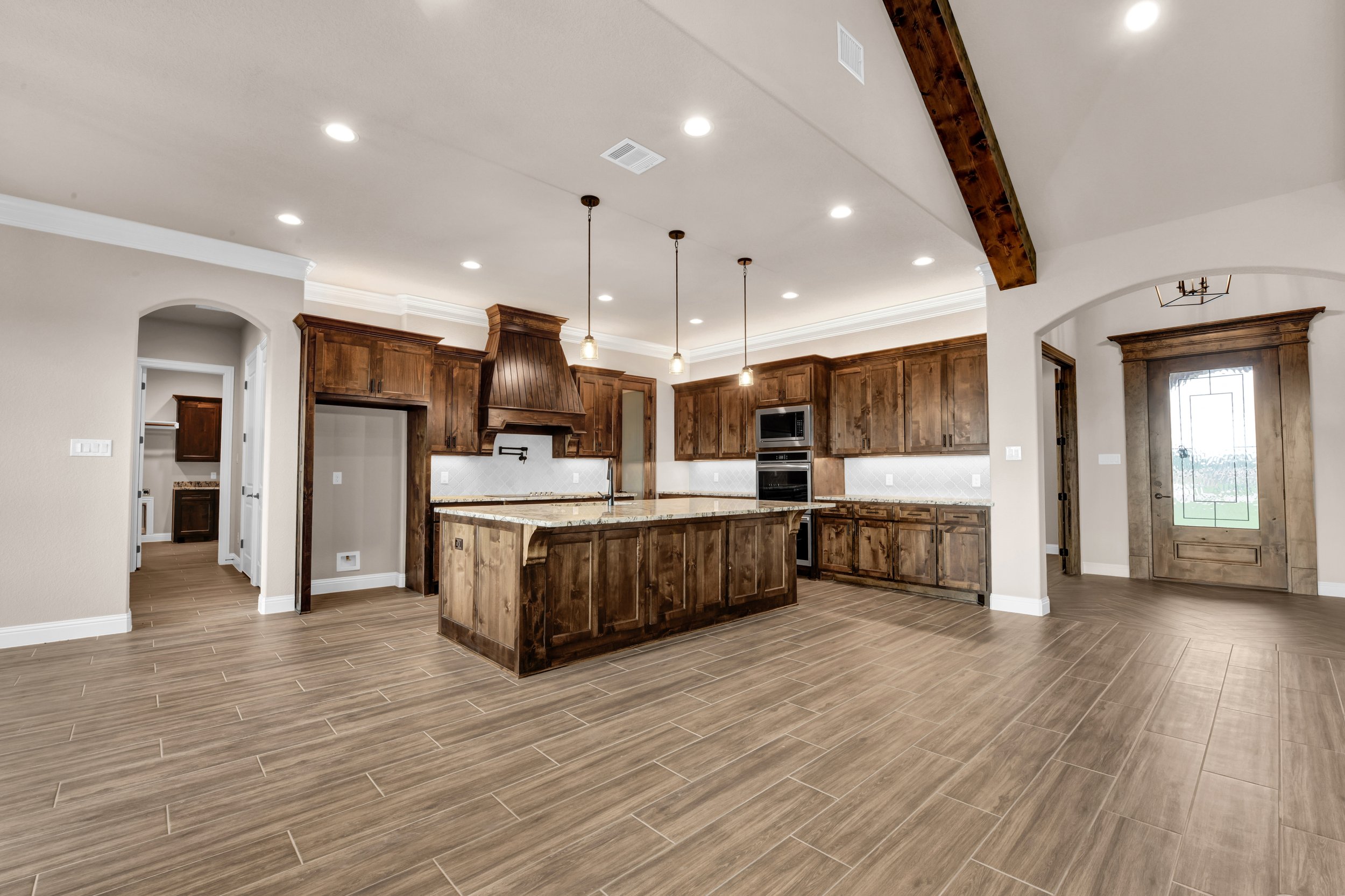 Spacious kitchen with wooden cabinets, a large island with a granite countertop, pendant lights hanging above, and a door with glass panel leading outside.