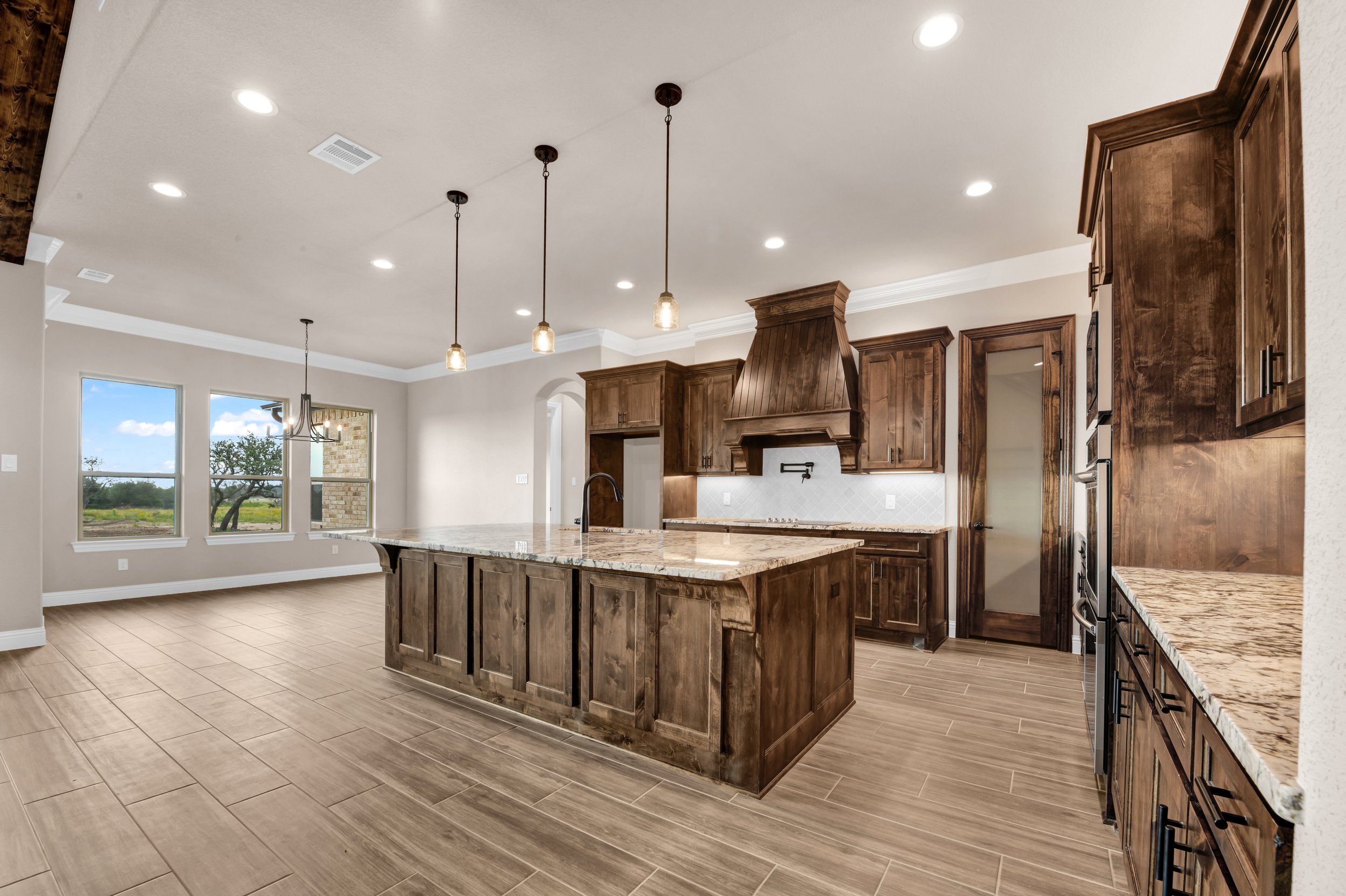 Modern kitchen with wooden cabinets, granite countertops, a kitchen island, and large windows overlooking a green yard.