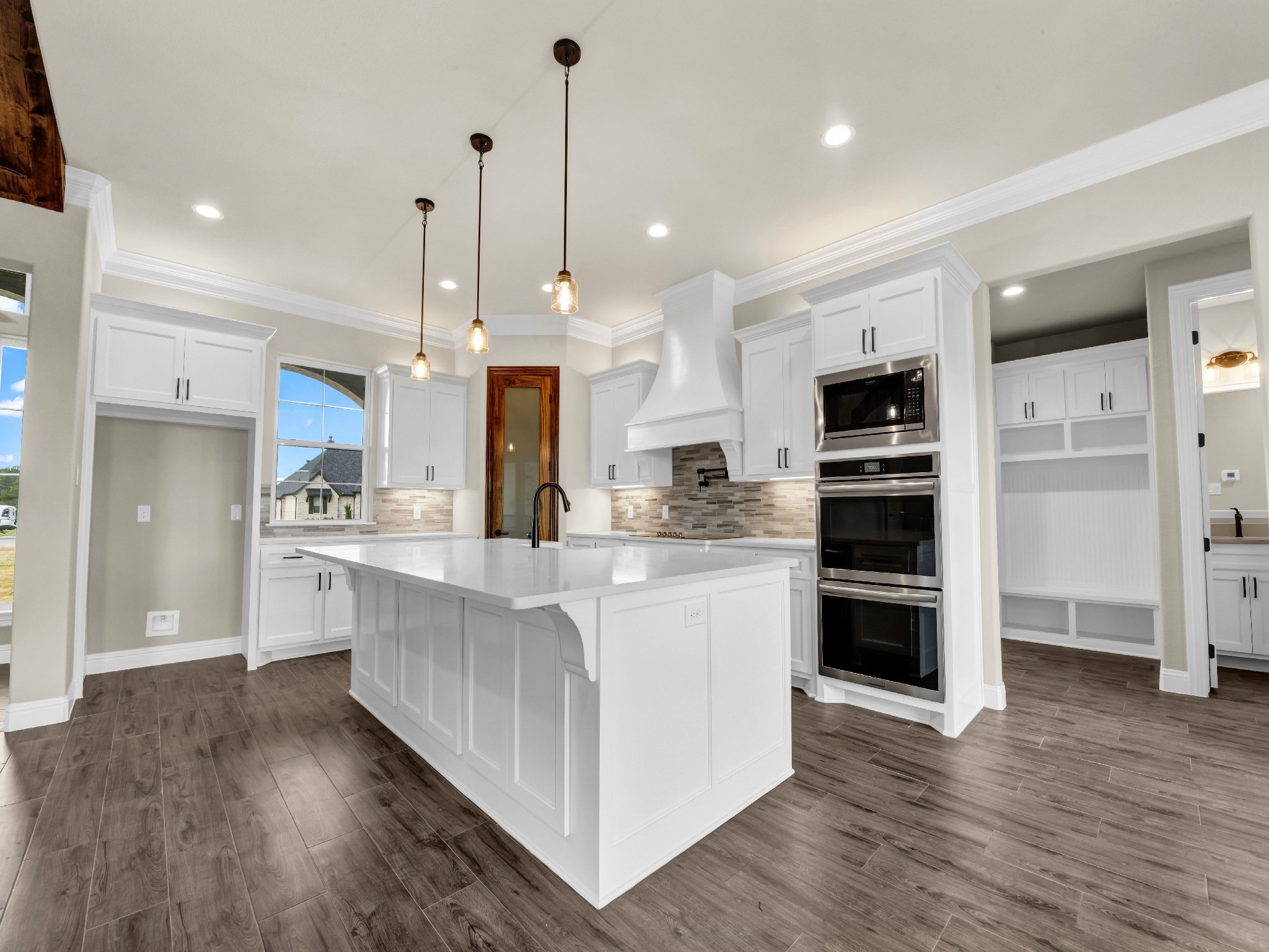 Modern kitchen with white cabinets, a kitchen island, stainless steel wall ovens, hardwood floors, pendant lights, and large windows.