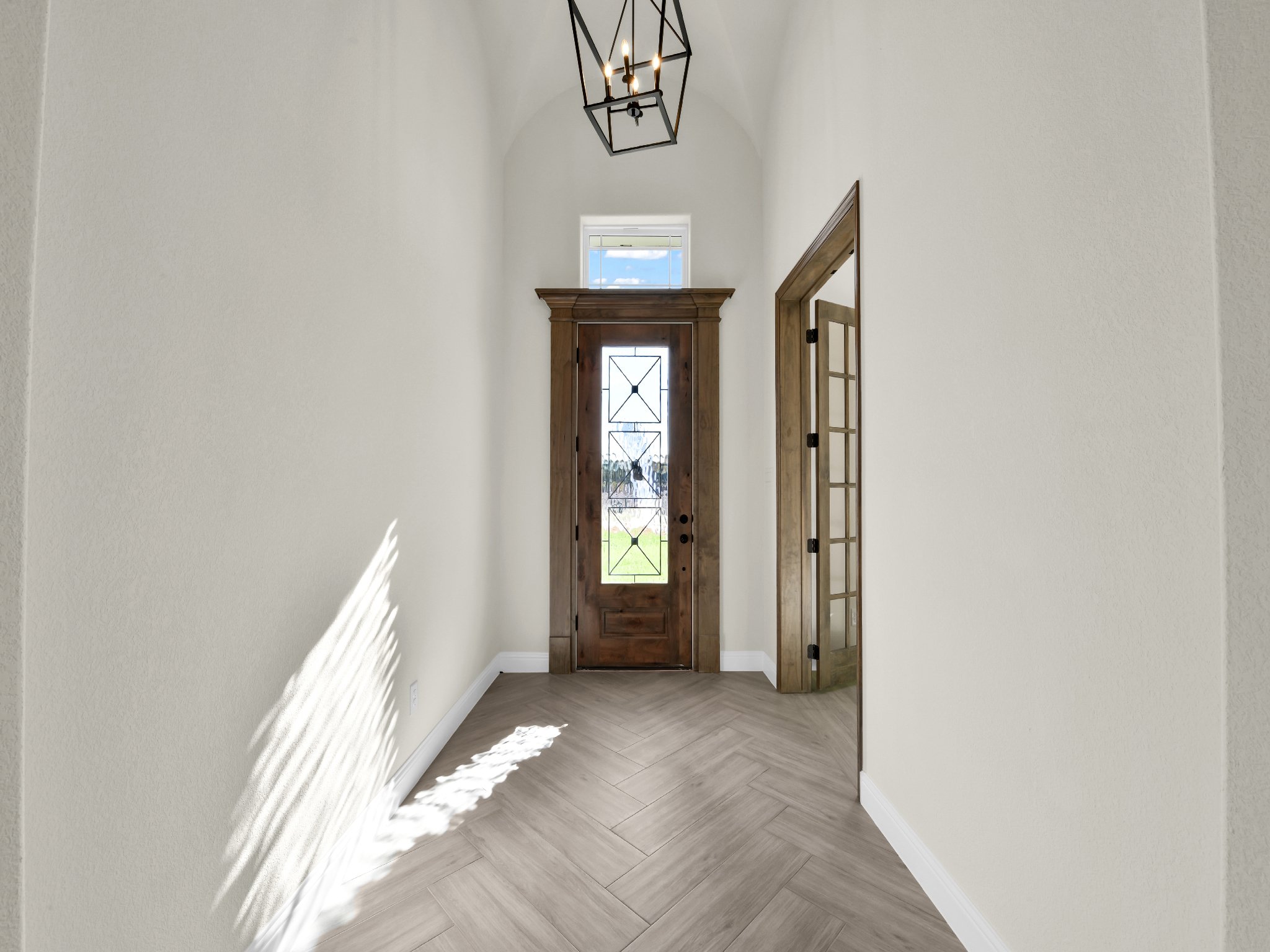 Entryway with a wooden front door, light-colored walls, herringbone wood flooring, and a black geometric pendant light fixture.