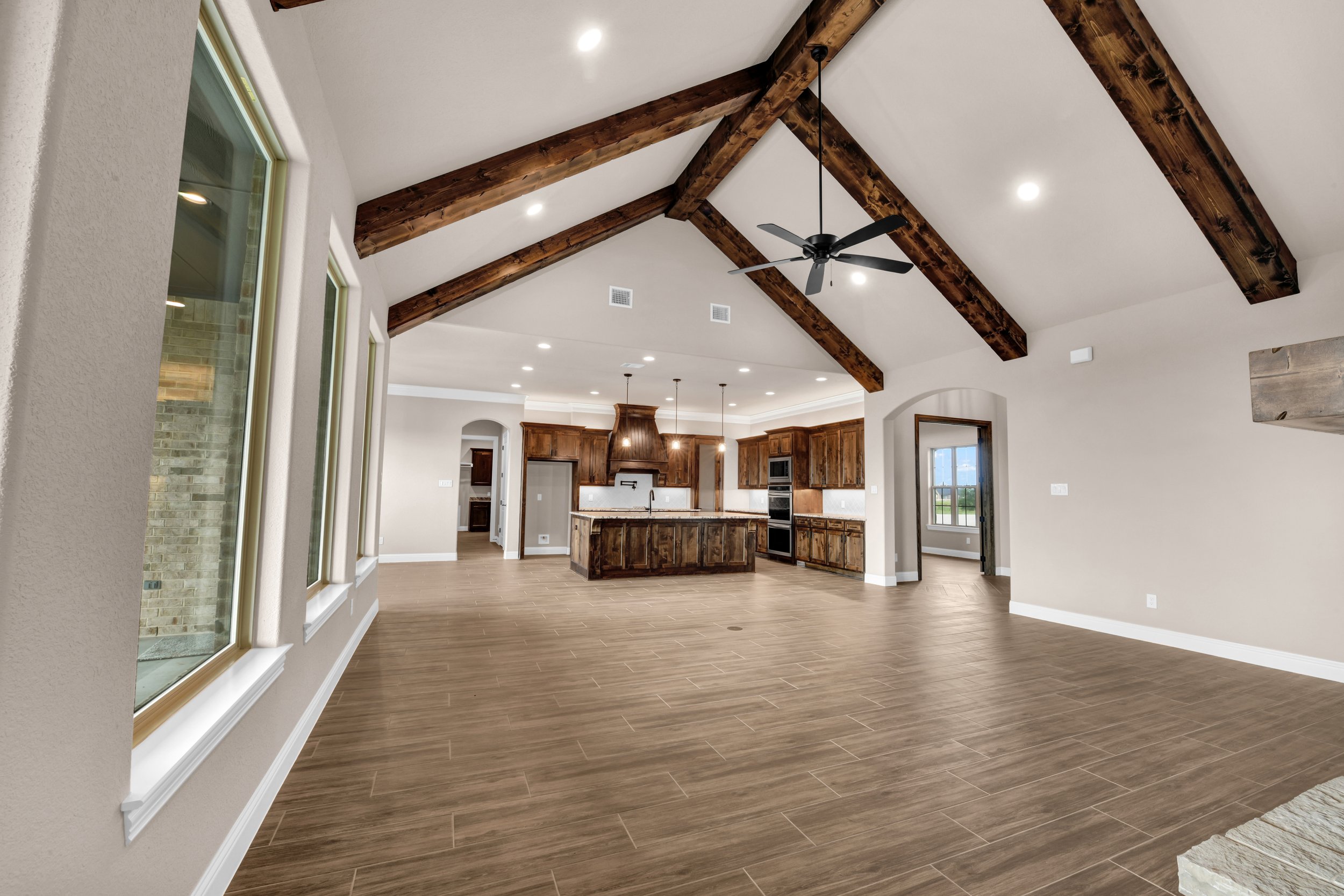 Open-concept living space with vaulted ceilings, exposed wooden beams, large windows, hardwood floors, and a modern kitchen with a central island.