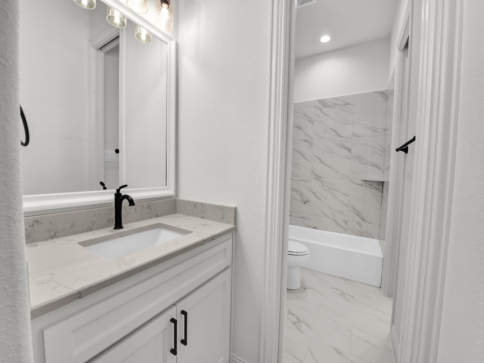 Modern bathroom with white vanity and black faucet, mirror, and marble tiling in shower area.