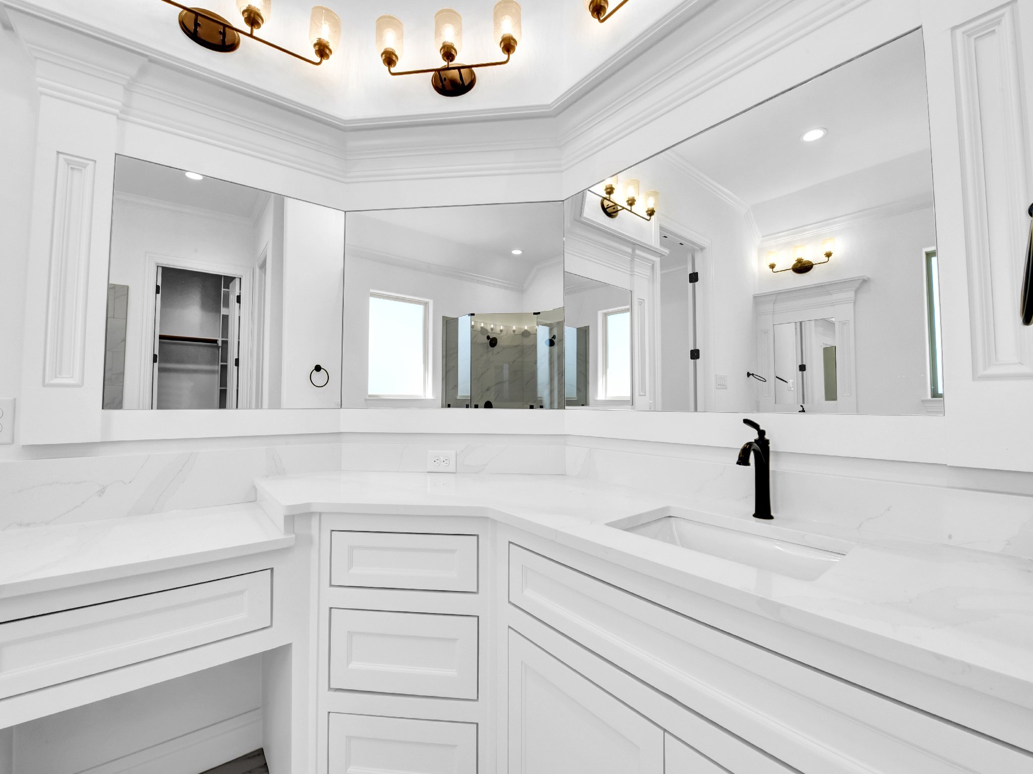 Modern white bathroom with black fixtures, a large mirror, and a shower area with glass doors.