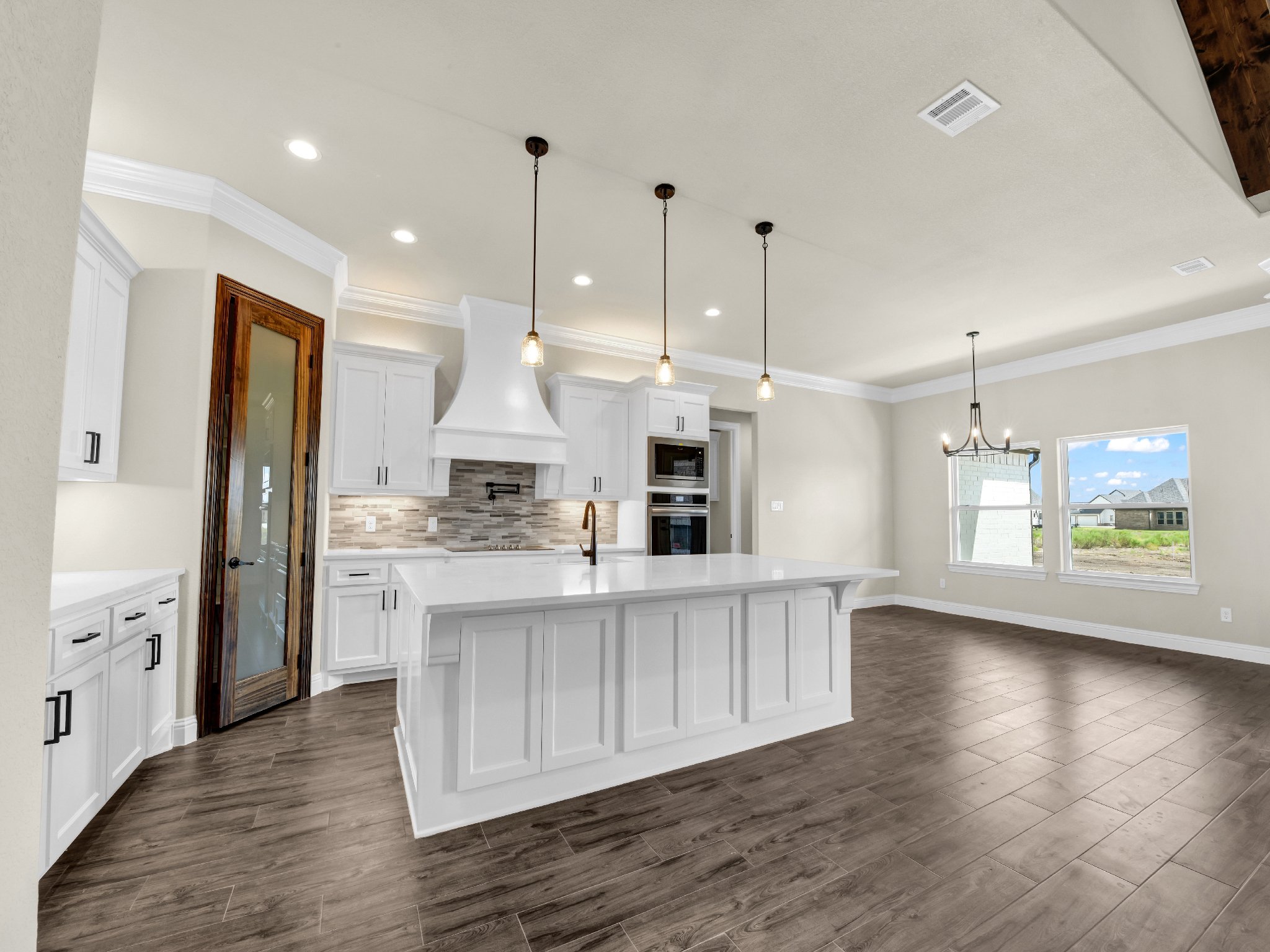Modern kitchen with white cabinets, a large island with a white countertop, pendant lighting, a built-in oven and microwave, large windows, and hardwood floors.
