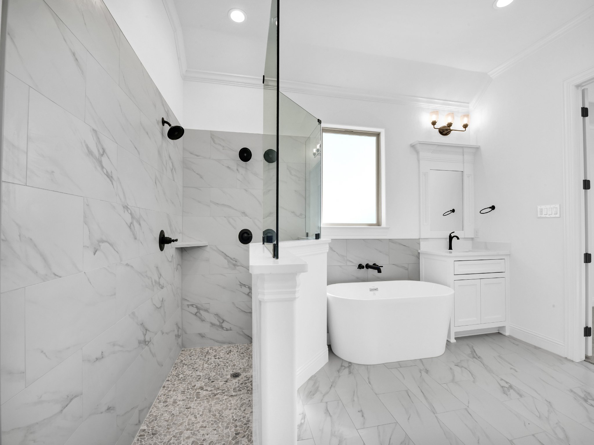Modern white bathroom with marble tiles, a walk-in shower with black fixtures, a bathtub, a white vanity with black hardware, a window on the wall, and a light fixture on the ceiling.