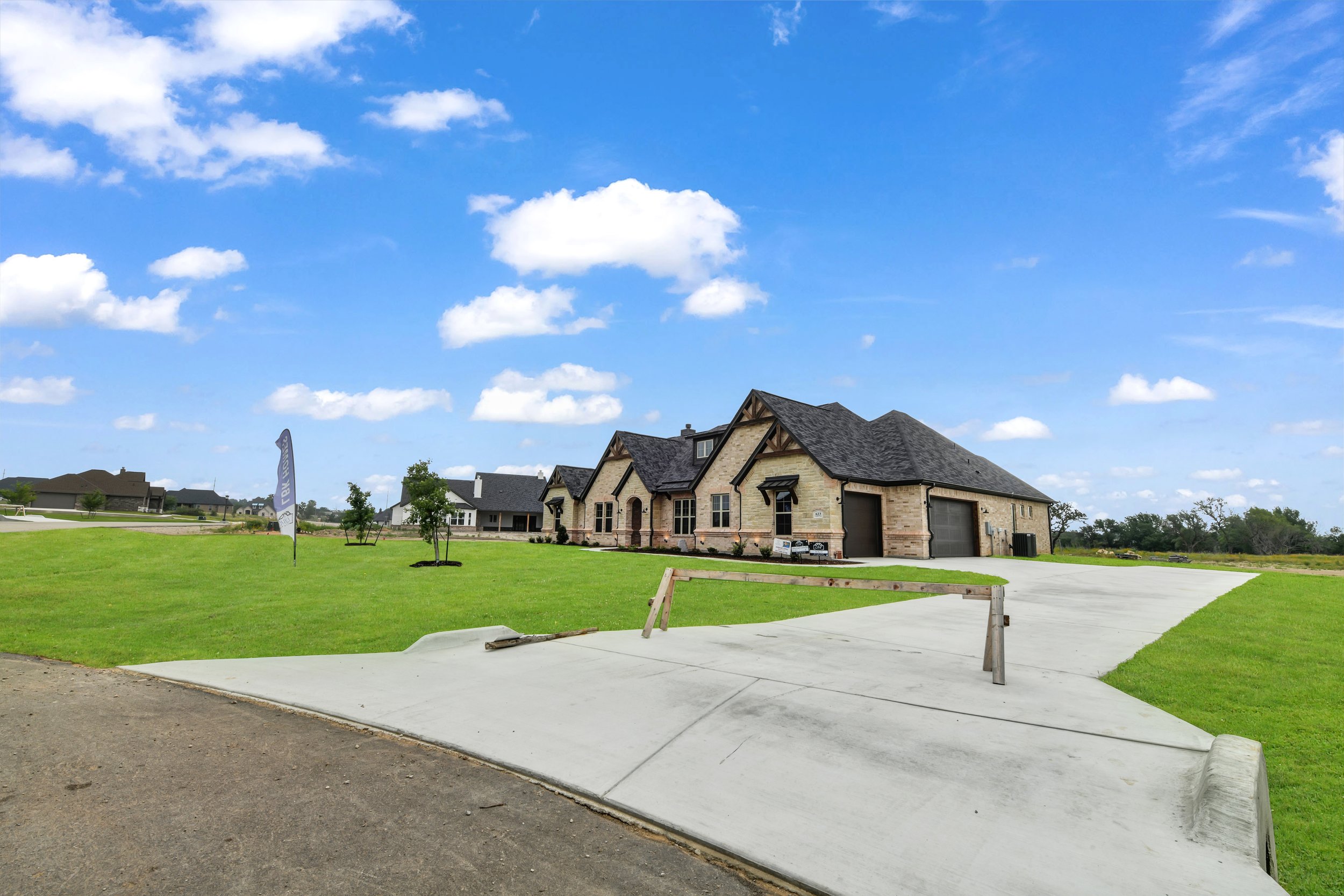 Newly built house with a stone and brick exterior, three garage doors, and a driveway in a suburban neighborhood under a partly cloudy sky.
