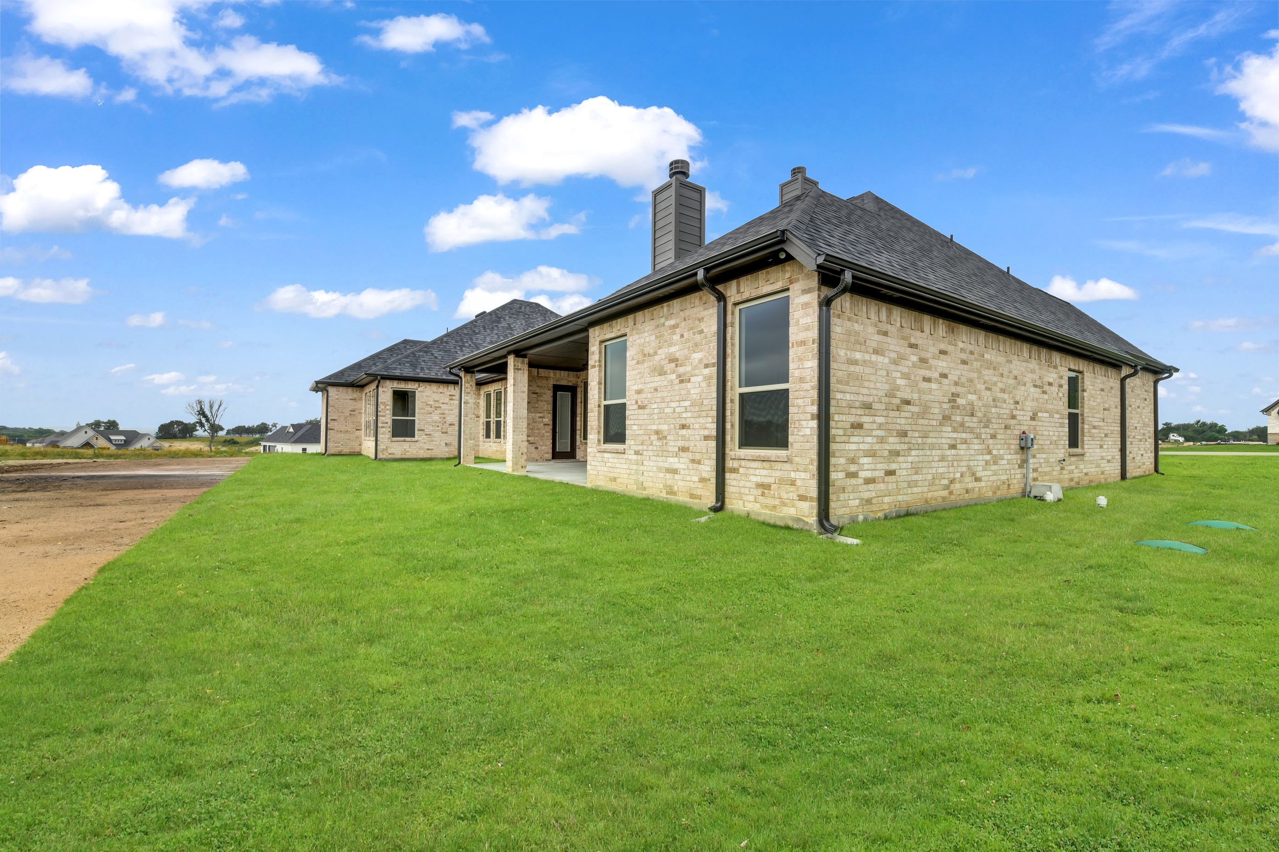 Newly constructed brick house with black roof and gutters, green lawn, and a partly cloudy blue sky.
