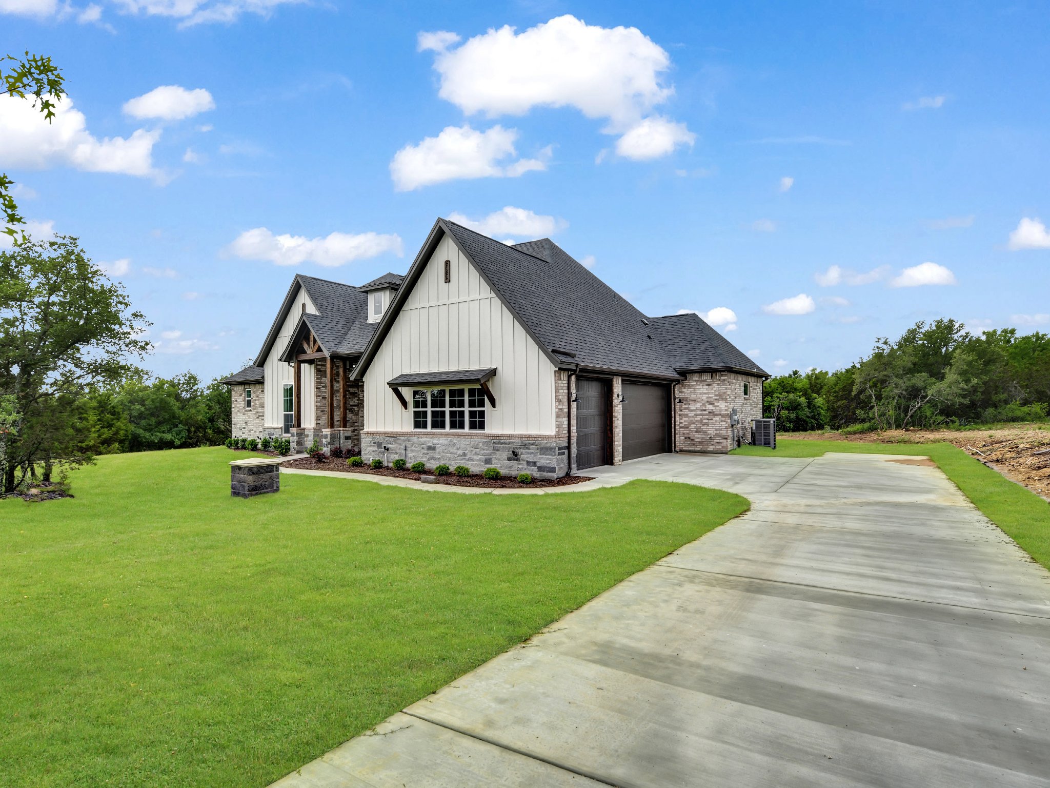 A modern suburban house with a lawn, driveway, and a partly cloudy blue sky.