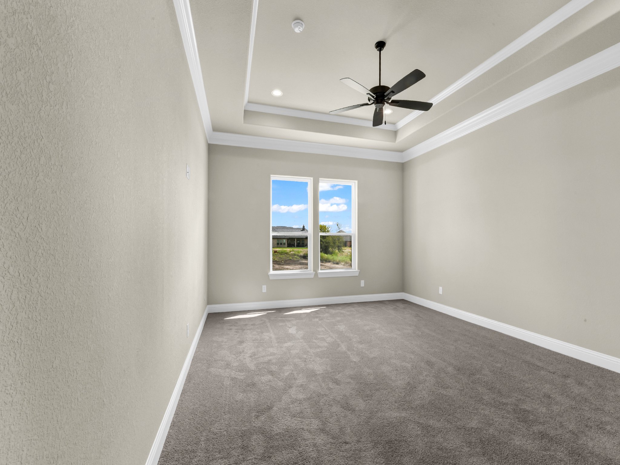 Empty room with beige walls, carpeted floor, two windows, white crown molding, and a black ceiling fan.