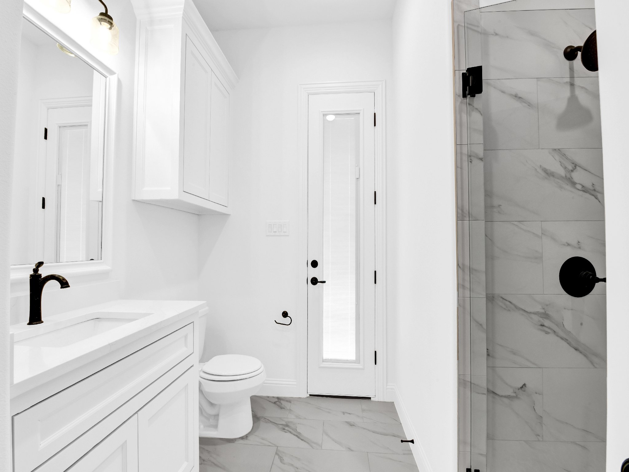 Modern white bathroom with a vanity sink, mirror, toilet, and a walk-in shower with marble tiles.