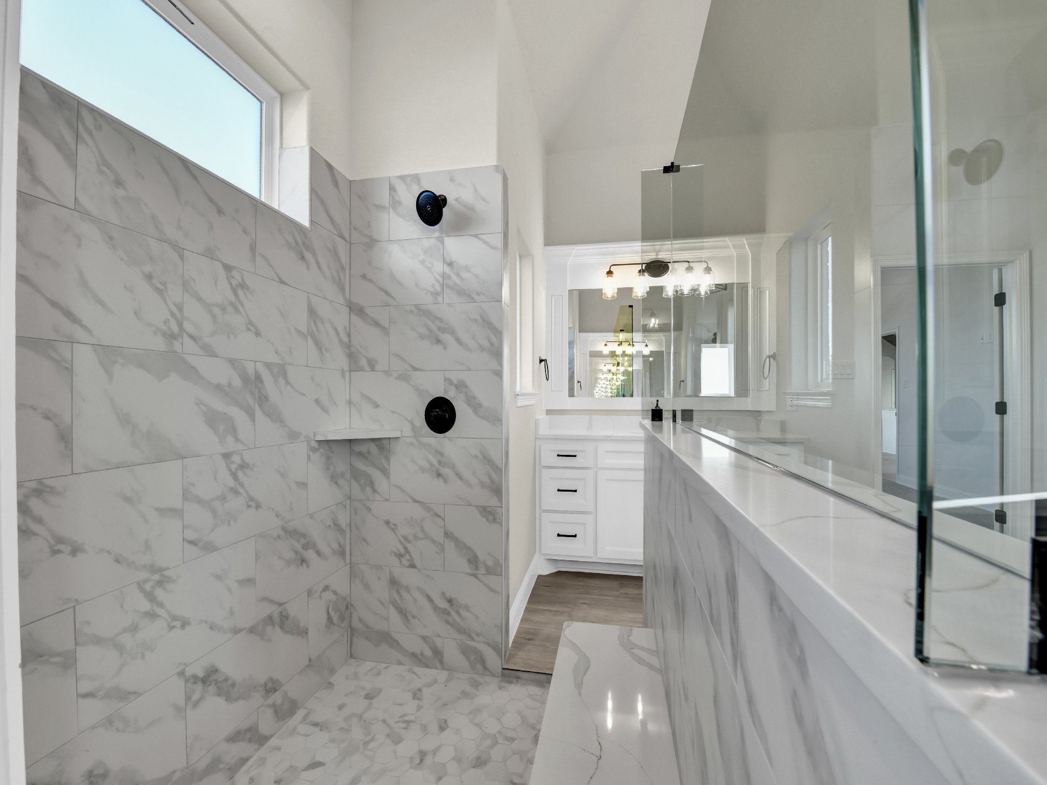 Modern bathroom with marble shower, white vanity, large mirror, and glass shower door
