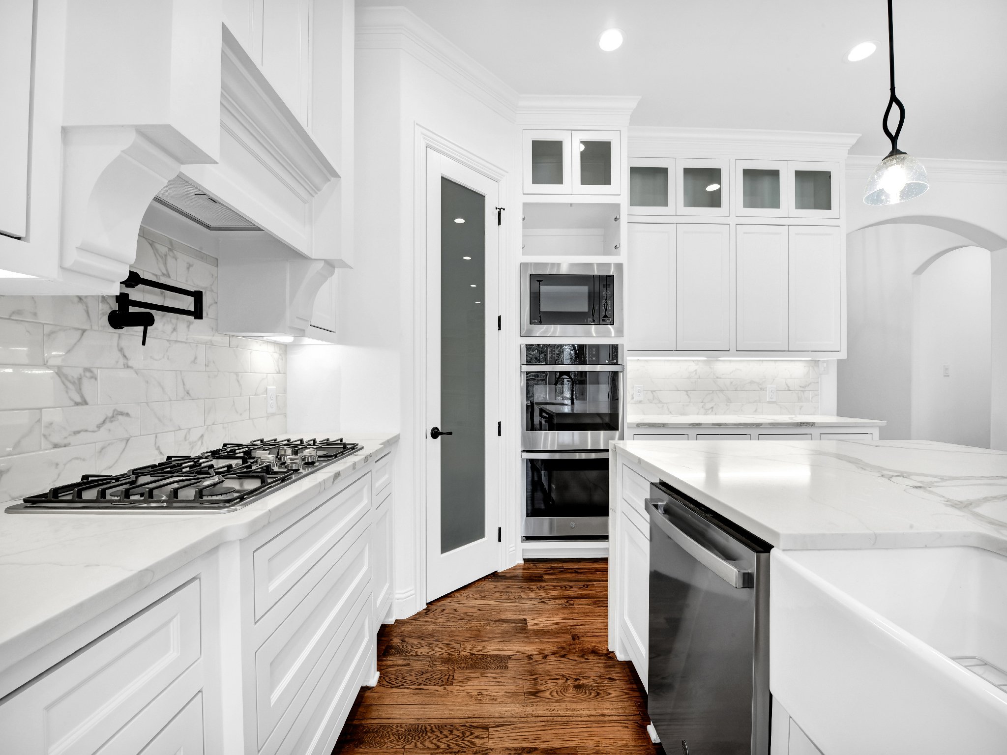 Modern white kitchen with marble countertops and backsplash, stainless steel appliances, and hardwood flooring.