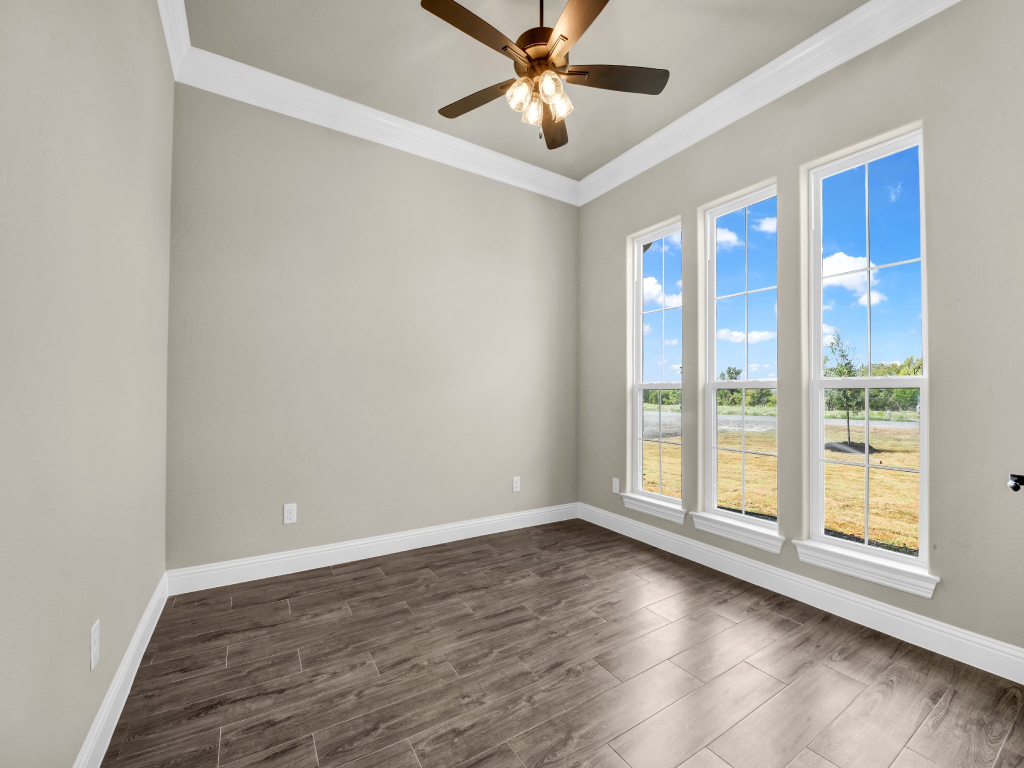 Empty room with beige walls, white trim, and large windows revealing a grassy outdoor landscape.