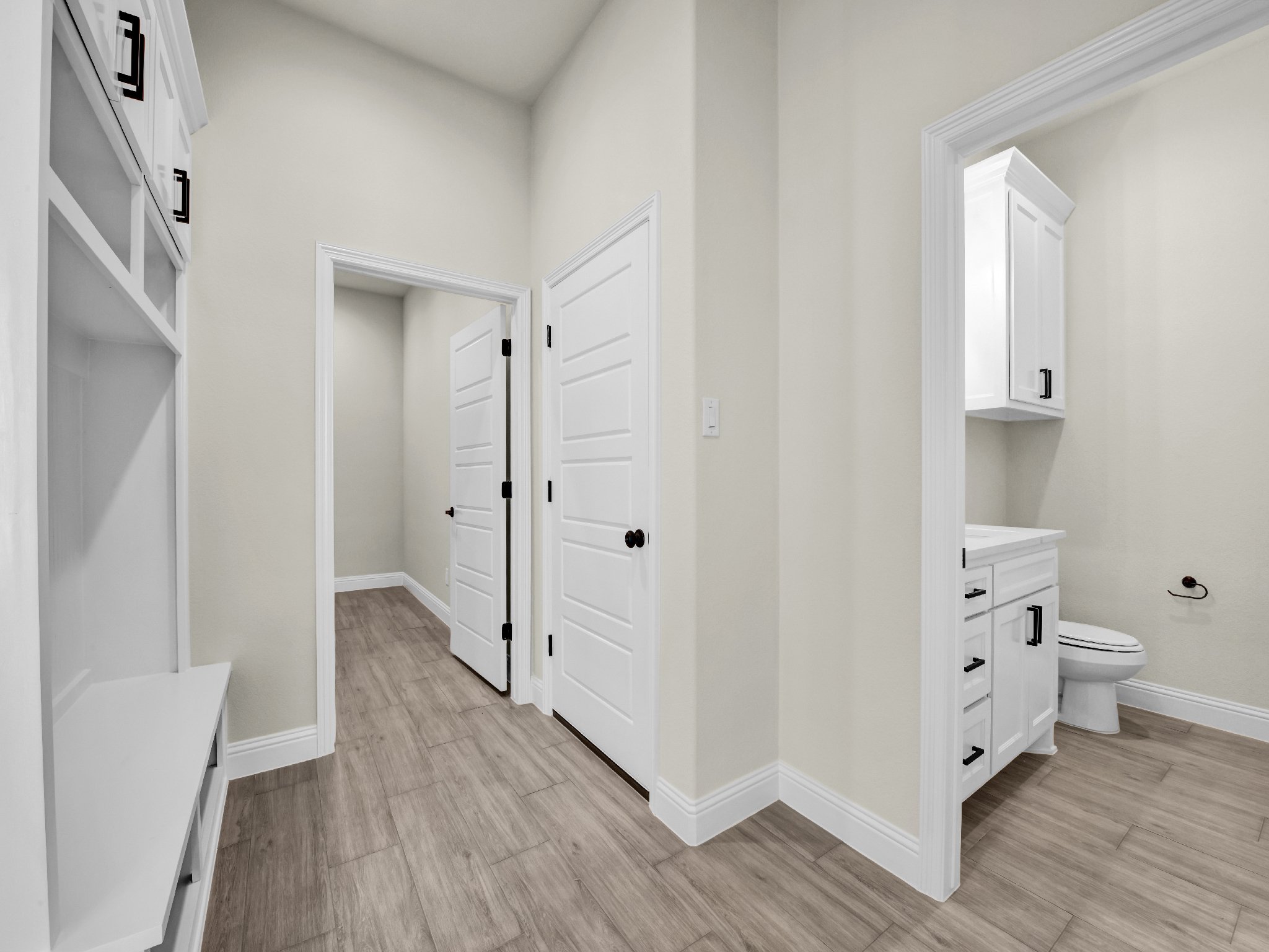 Empty room with white walls, wooden flooring, and a partial view of a bathroom with a toilet and cabinet.