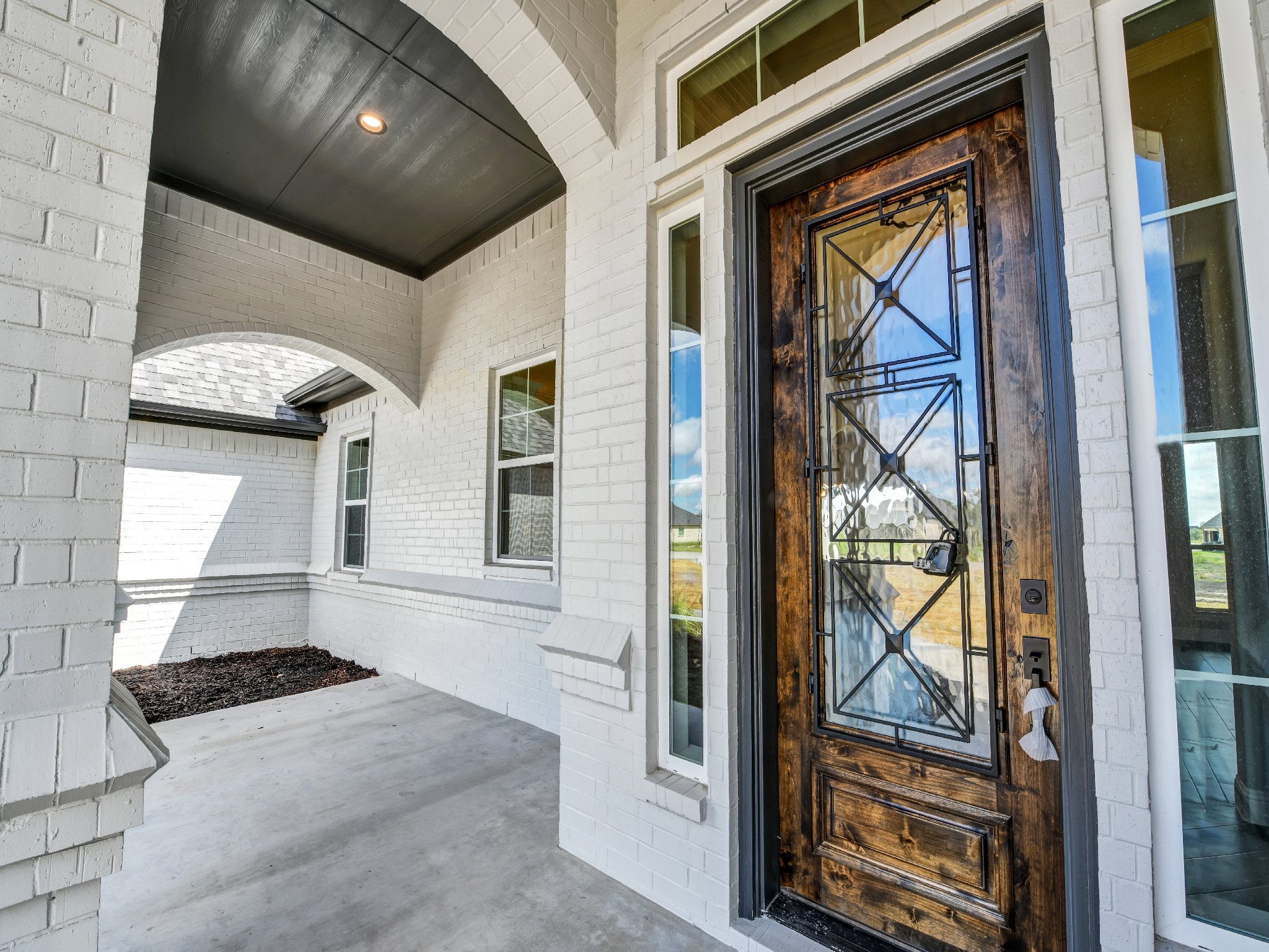 Close-up of a wooden front door with decorative ironwork on a white brick house exterior, with large glass panels and windows
