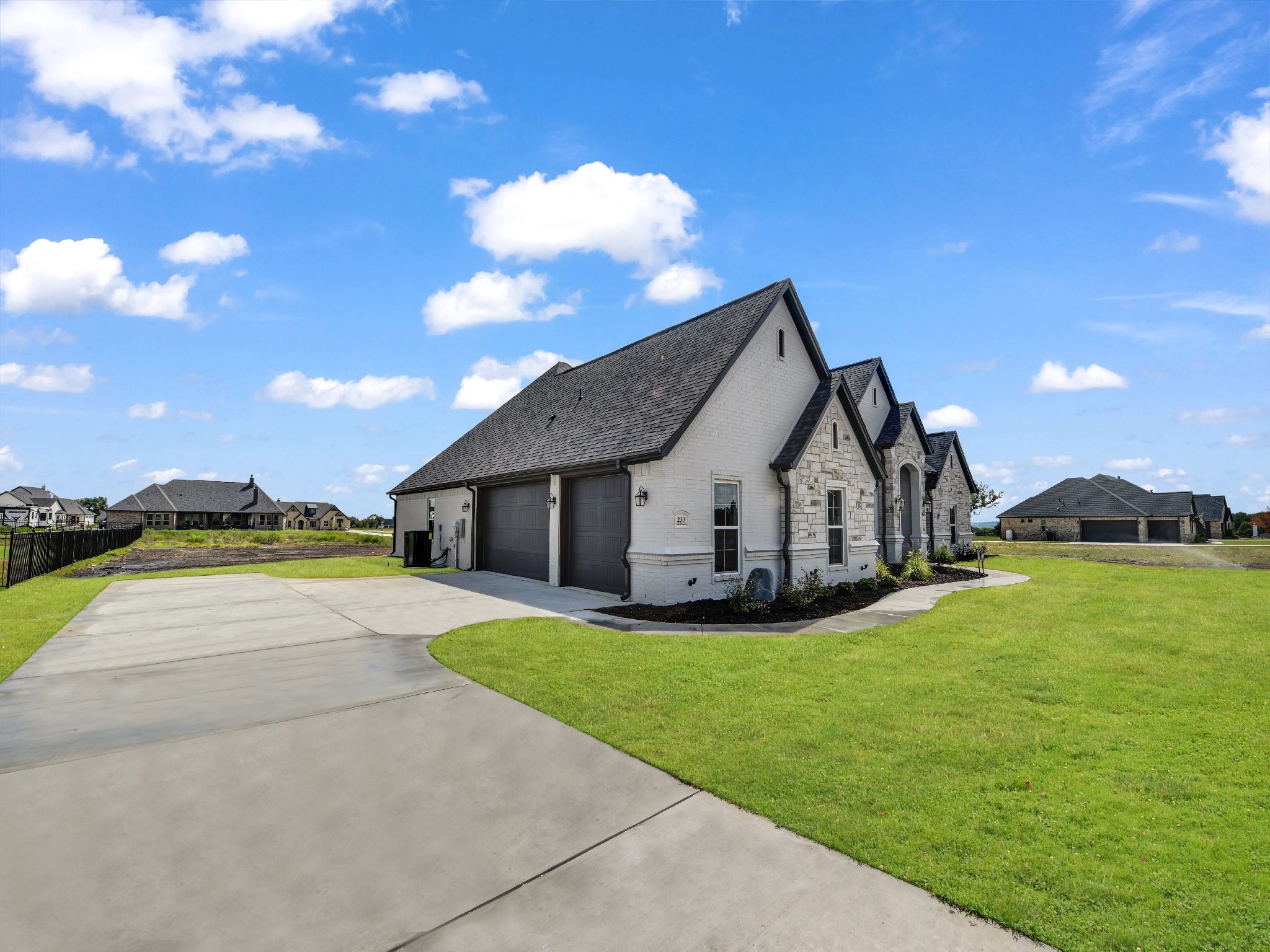 Newly built white brick house with attached garage, surrounded by green lawn and a clear blue sky with scattered clouds.