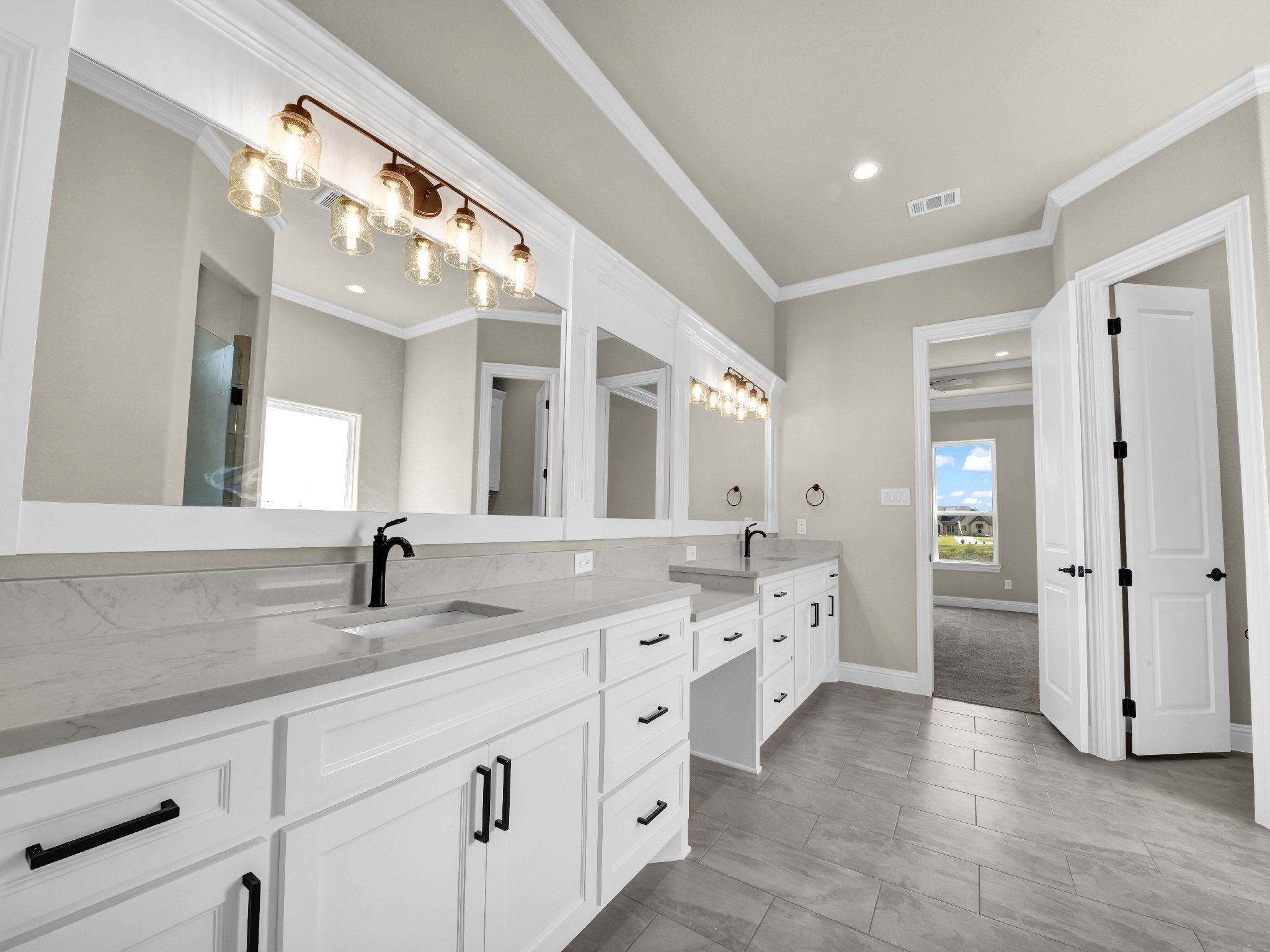 Modern bathroom with double vanity, large wall mirror, black fixtures, beige walls, and gray tiled flooring.