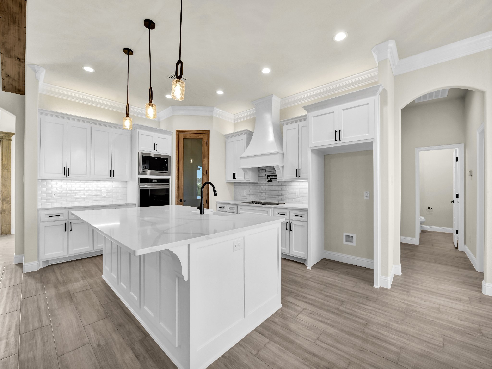 Modern kitchen with white cabinets, black hardware, large island with black faucet, wood flooring, and pendant lighting
