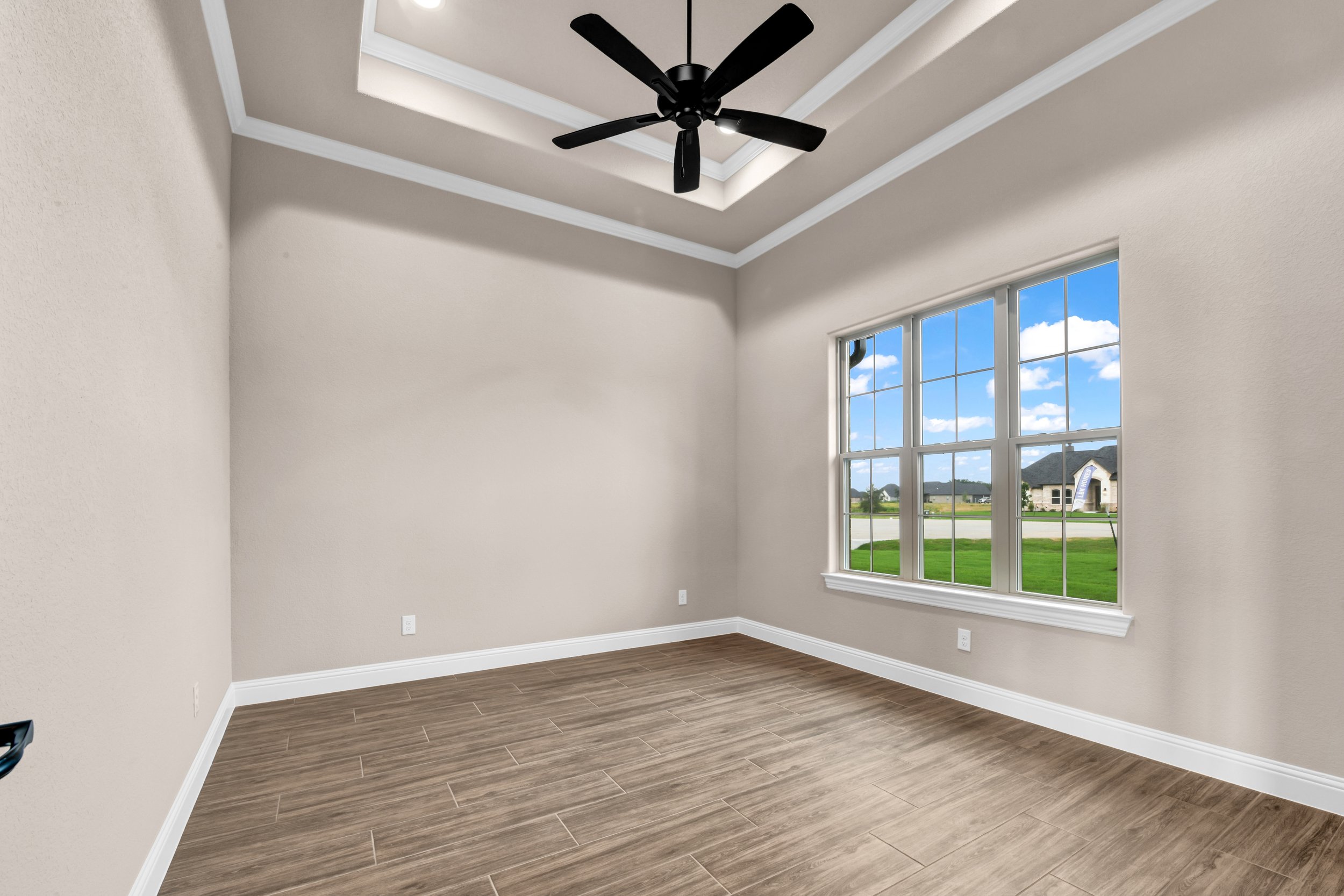 Empty room with large window, wood flooring, beige walls, and a ceiling fan.